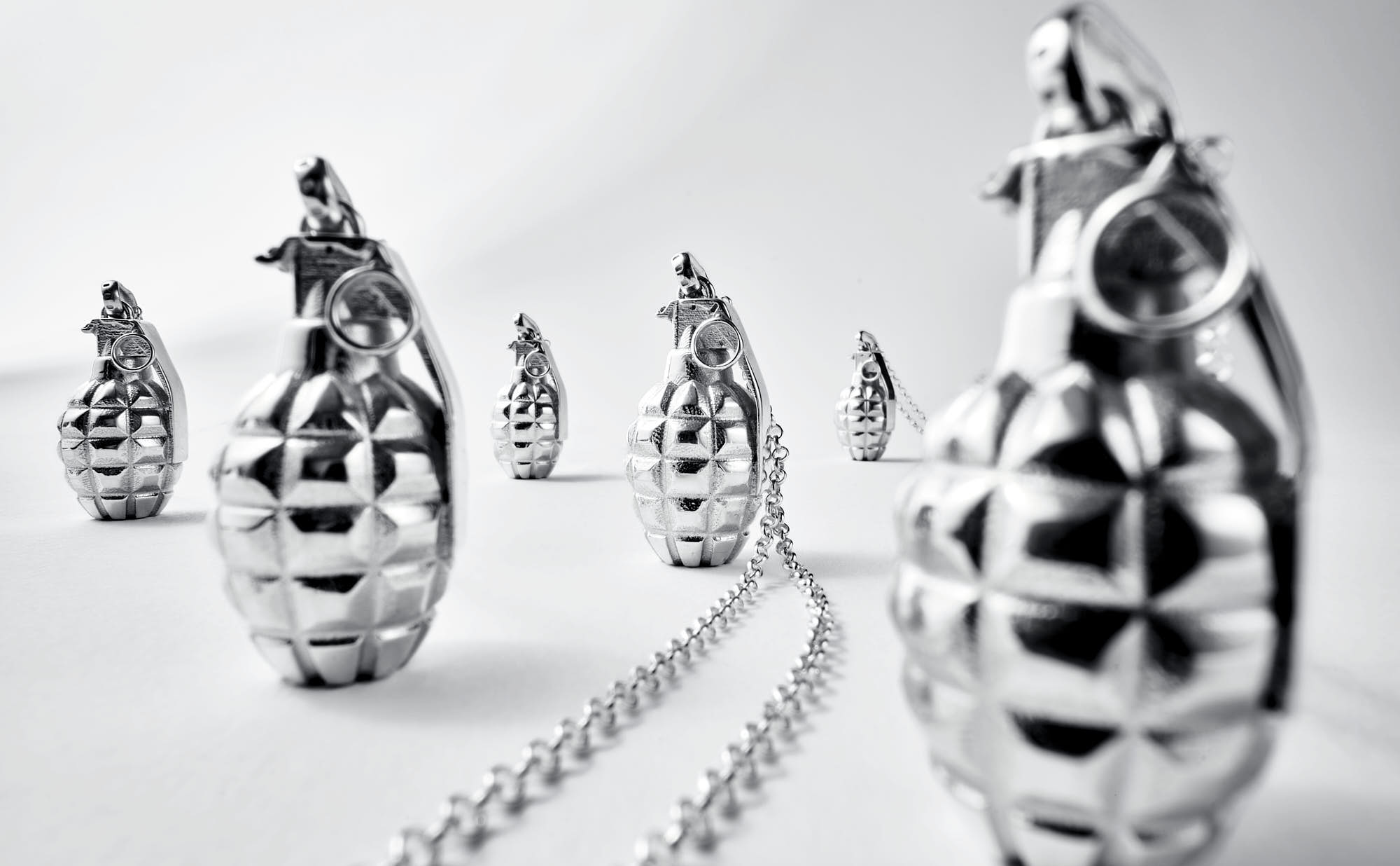 A surreal scene of metallic jewellery resembling grenades, arranged in an abstract landscape with light tones.