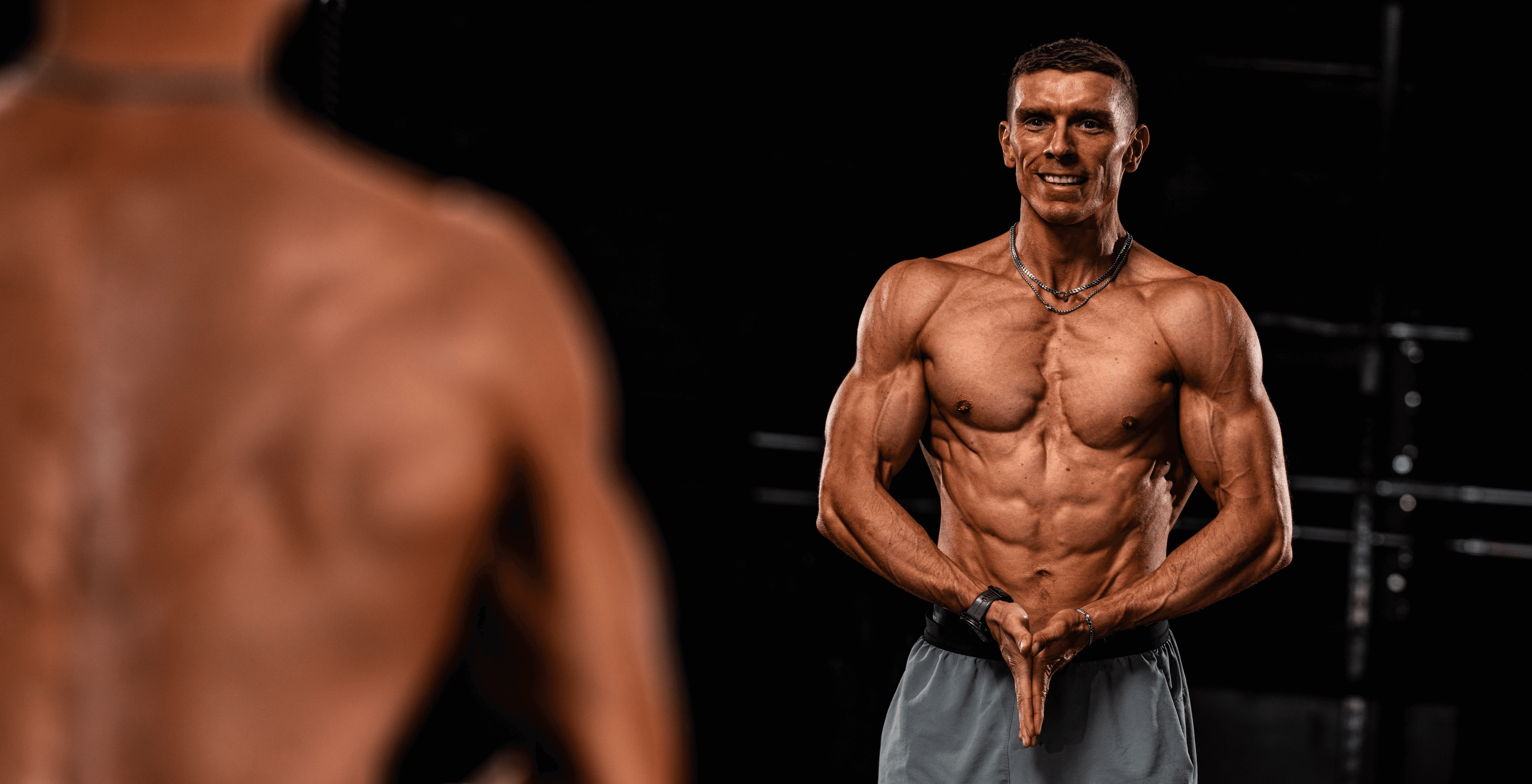 A personal coach lifts a heavy barbell in a dimly lit gym, focusing intently on the task.