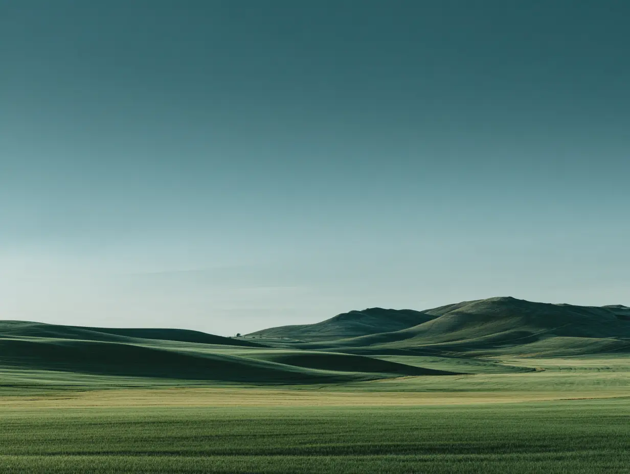 Rolling green hills stretch toward a distant mountain range under a clear, pale blue sky.