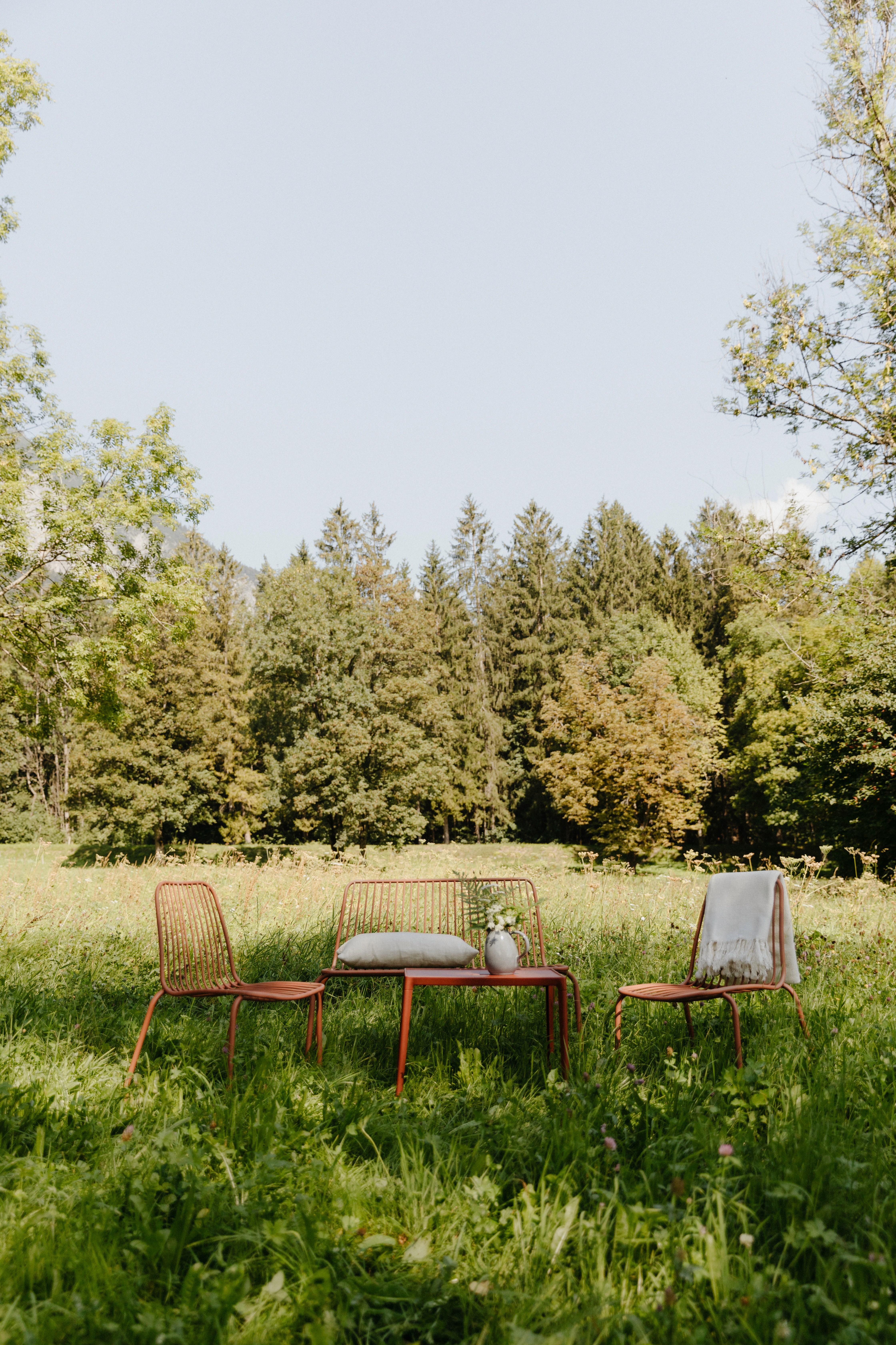 A seating area in the lush green medows with trees in the background.
