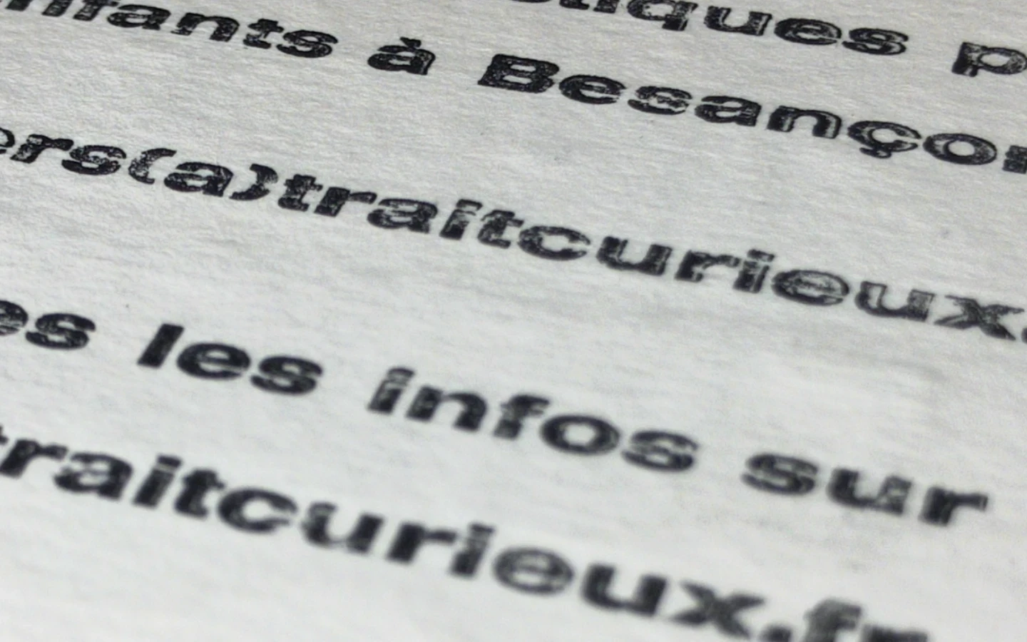 Gros plan sur le texte imprimé en typographie au plomb au verso de la carte Trait Curieux, relief des caractères visible en lumière rasante.
