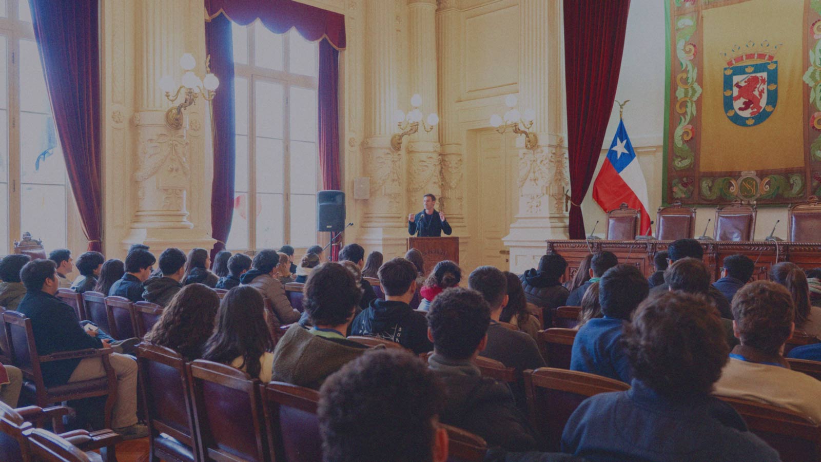 Portada de Chile nos llama, programa de formación de IdeaPaís, mostrando un auditorio con filas de jóvenes que escuchan sentados a un expositor. 