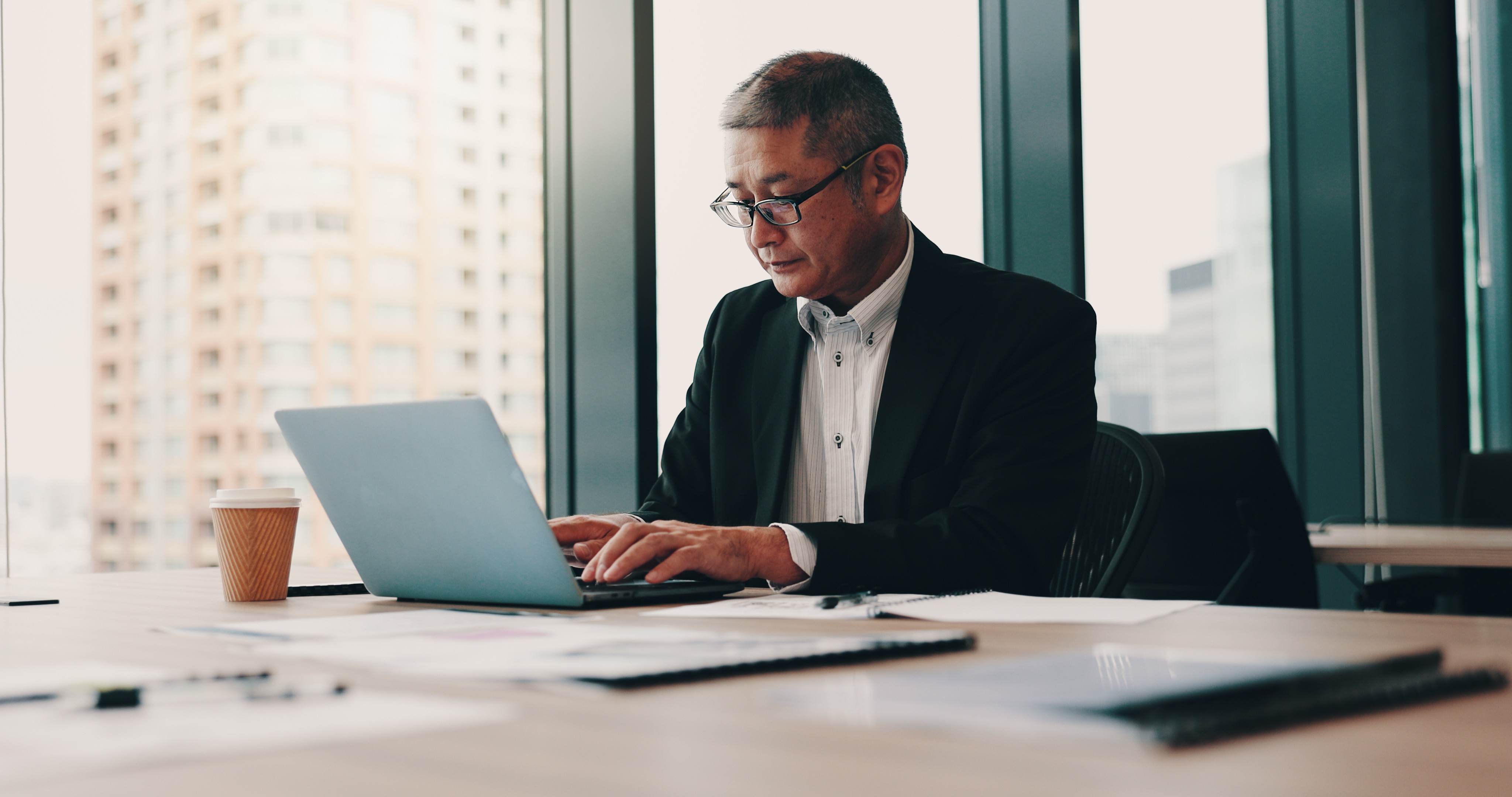 Senior professional working on a laptop in a modern office, reviewing documents at a desk, representing structured operational design, control implementation, and day-to-day execution in organisations.
