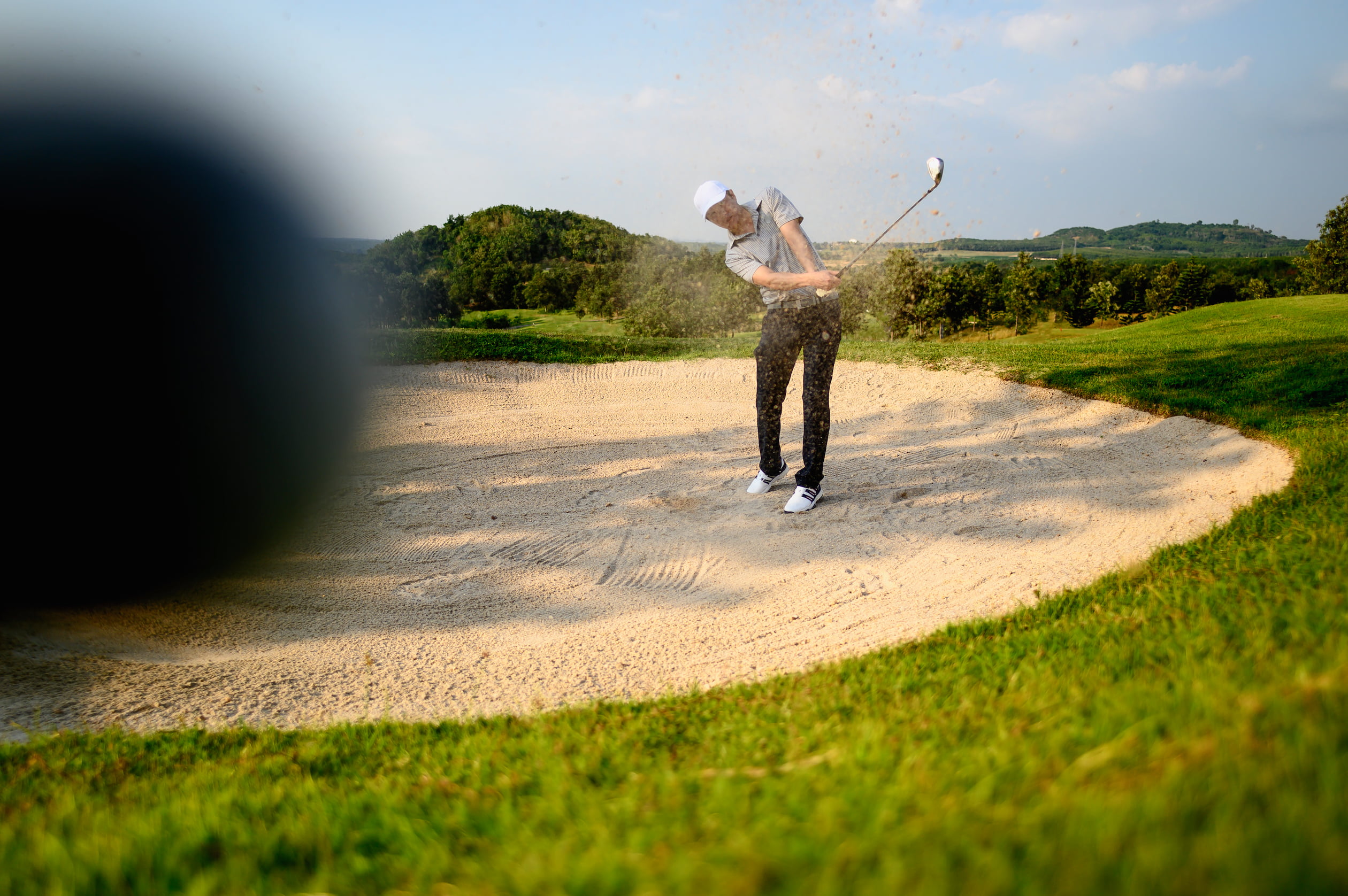 Golfer hitting a bunker shot during Pianeta Sport Golf Tour in a scenic countryside course"