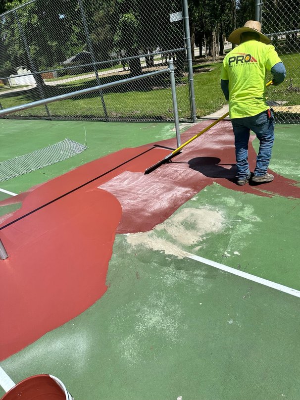 Crew resurfacing a tennis court with new coating materials