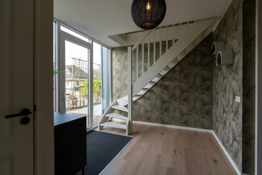 De entree van de vakantiewoning met een witte trap, een glazen voordeur en decoratief behang.