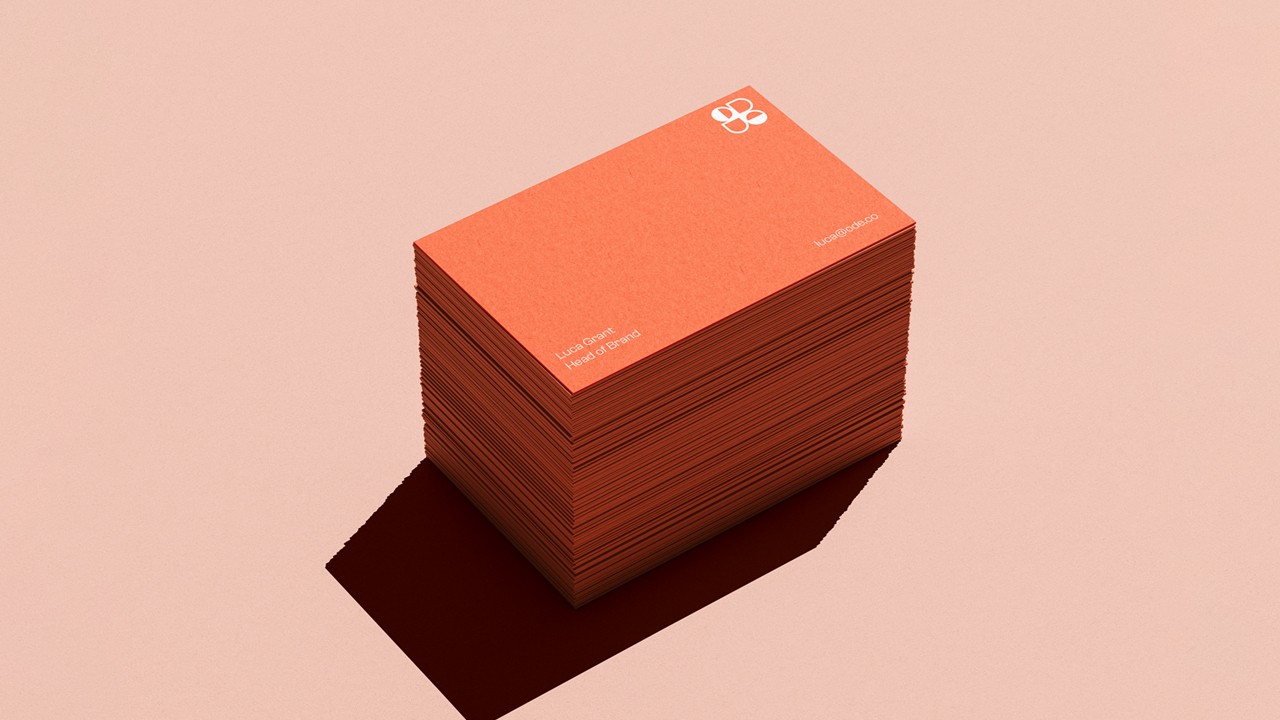 Tower of red-orange business cards on a peach surface, the top card displaying a white ODE logo in the top corner and small white contact details beneath.