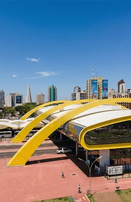 Ponto de embarque em Maringá com cobertura amarela, vias urbanas e edifícios ao fundo
