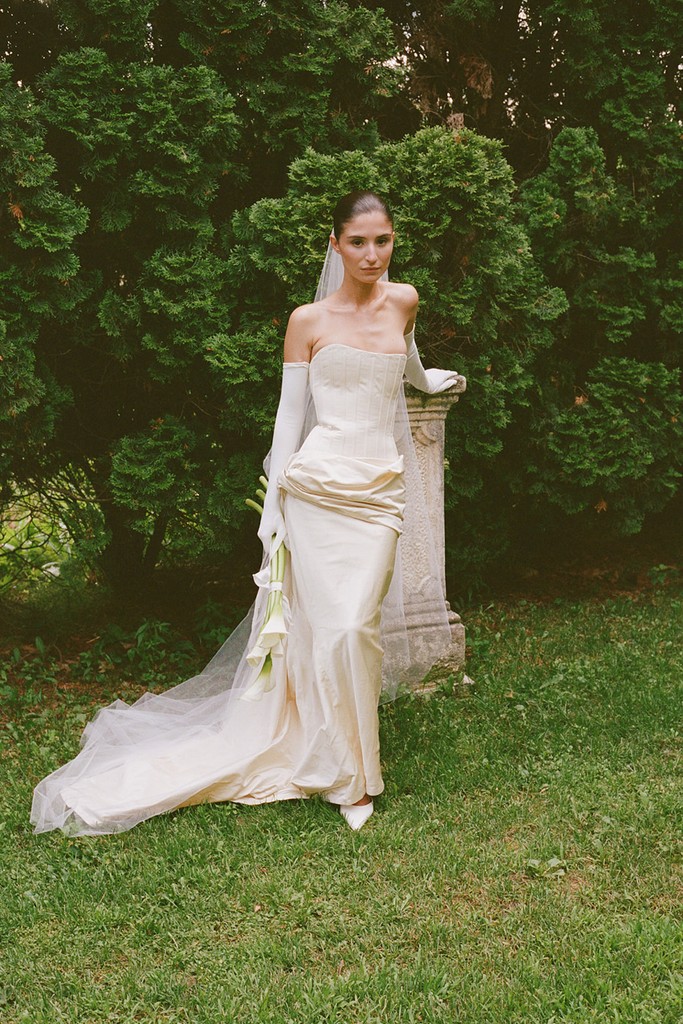 Bride in an elegant corseted wedding gown posing in a garden setting before the reception