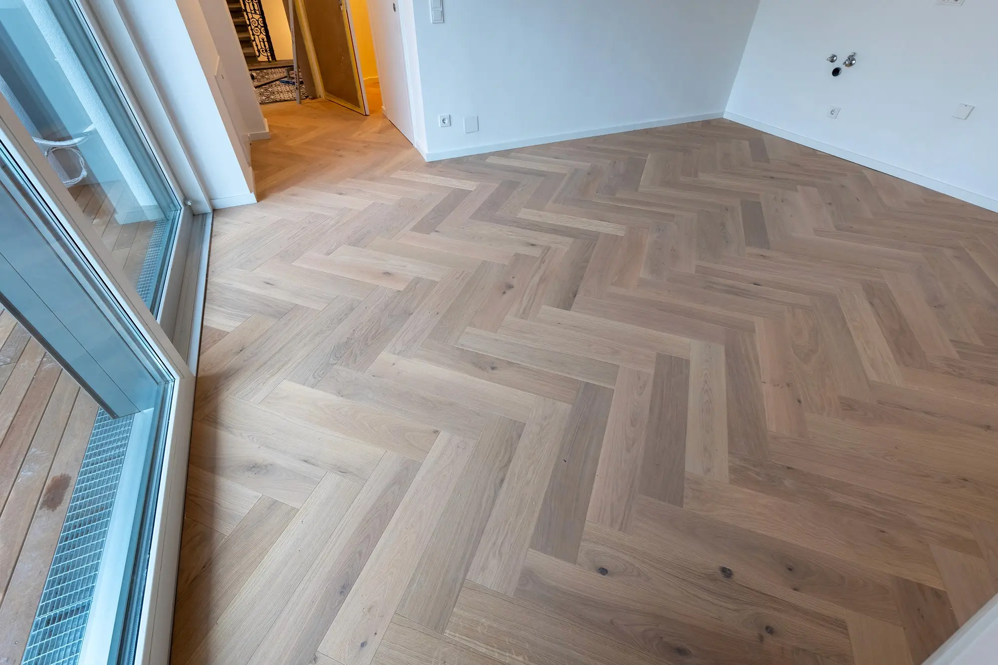 Großer Wohnraum mit bodentiefen Fenstern und neu verlegtem Fischgrät-Parkettboden