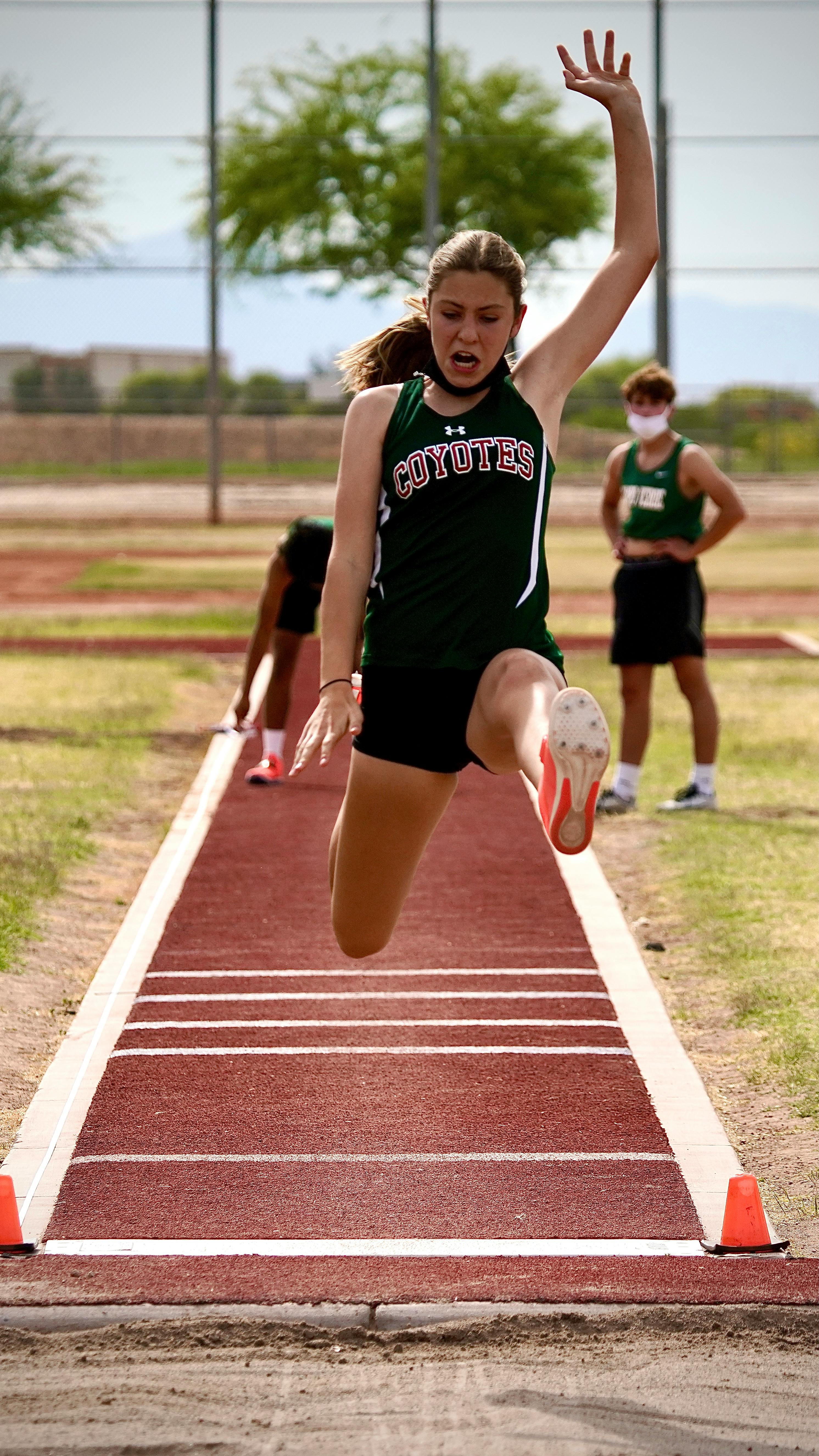 Young White female running the long jump mid-air