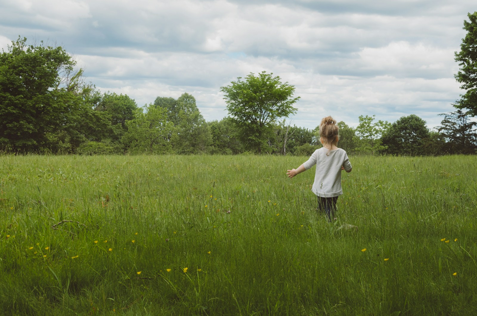 A child running away across a green meadow under a cloudy sky