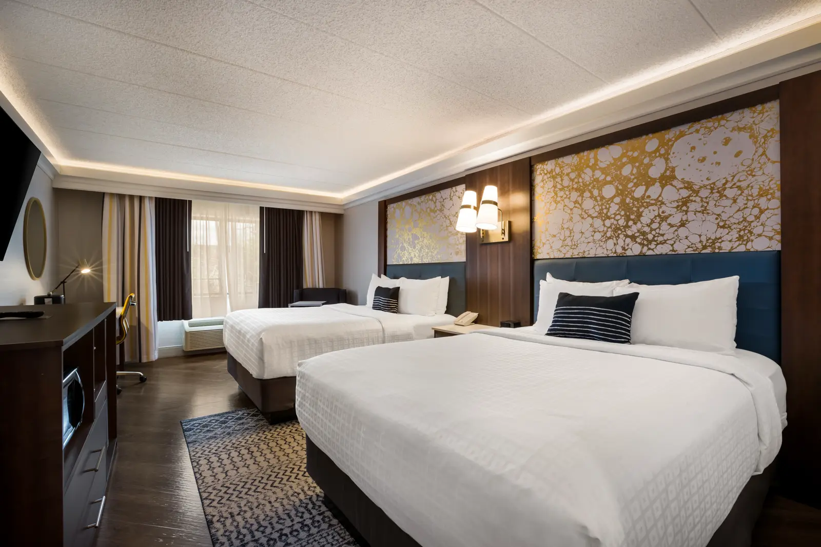 Hotel room with two beds, blue headboards, and gold marbled wallpaper.