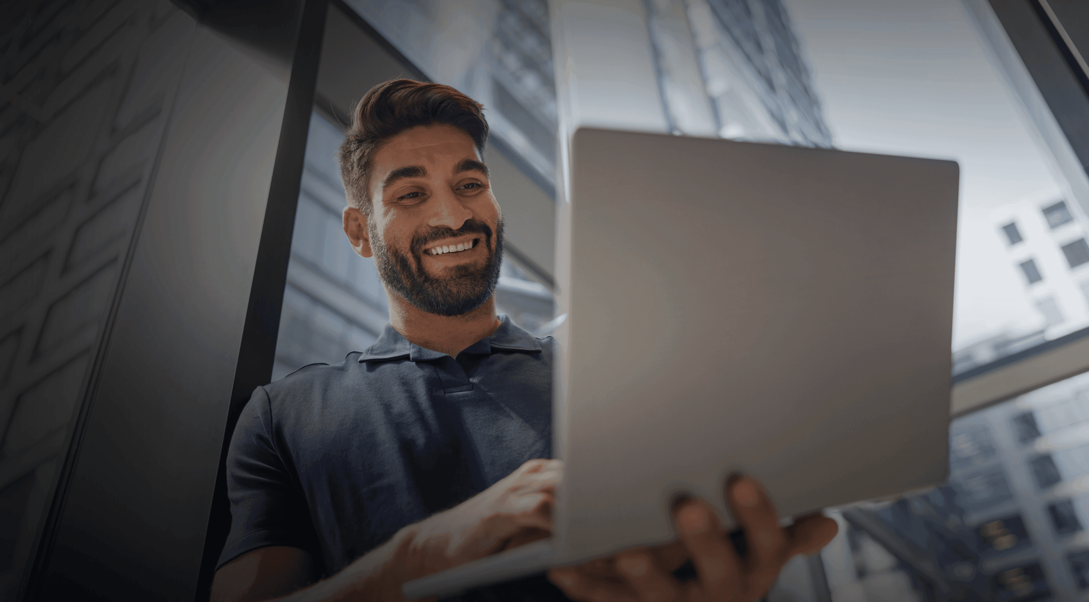 A young businessman in a blue shirt smiling at his laptop