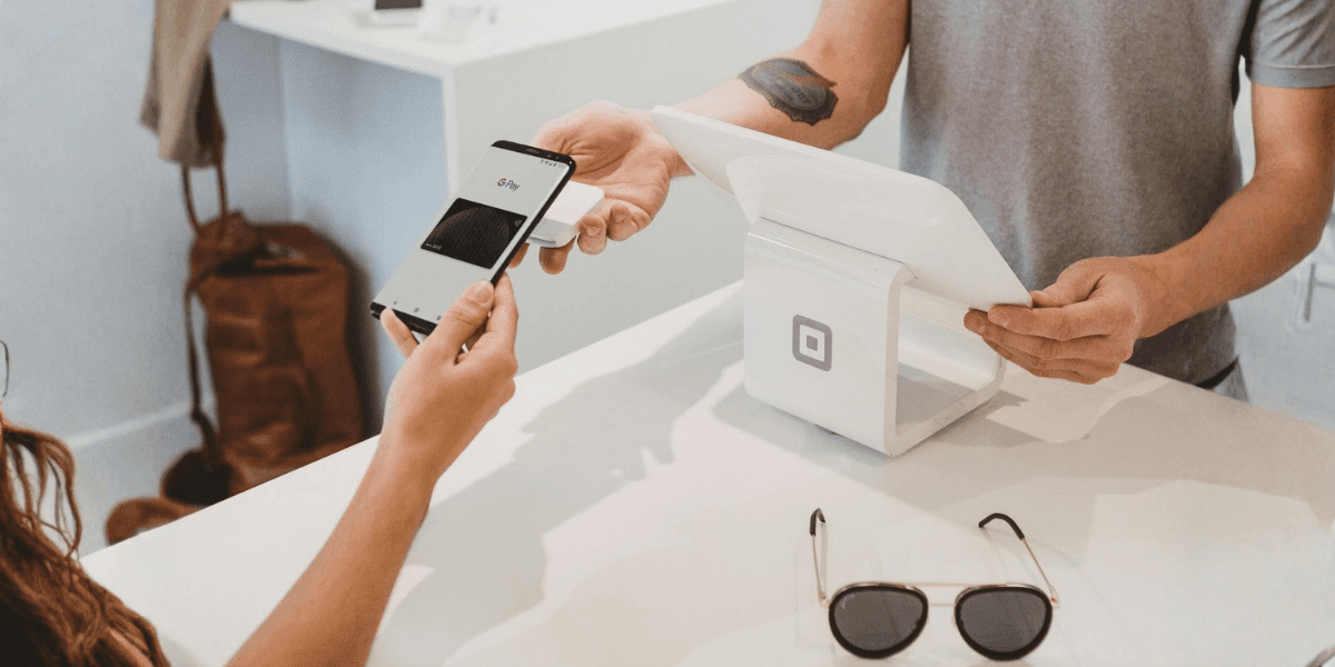 A person using Google Pay on their smartphone for a secure transaction at a point-of-sale terminal with Square.