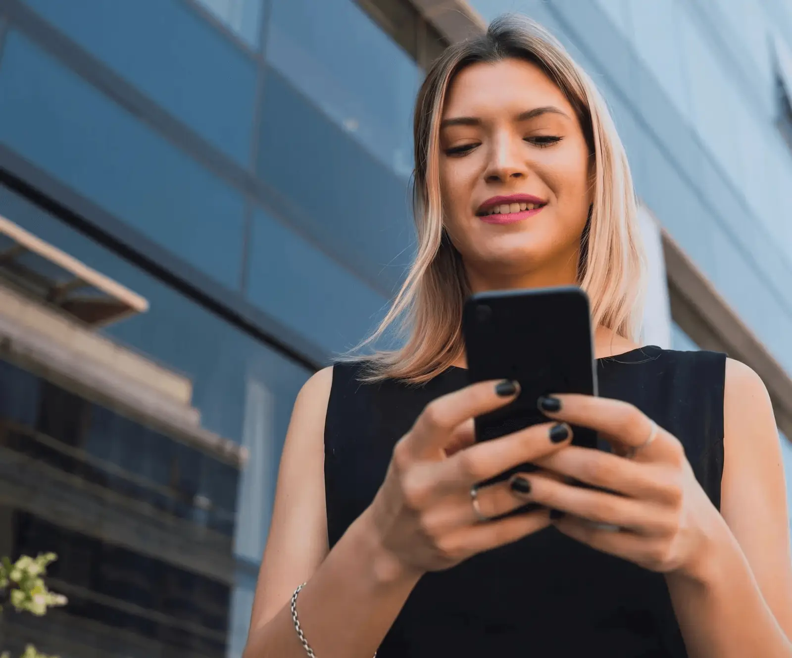 Mulher mexendo no celular em frente a um prédio