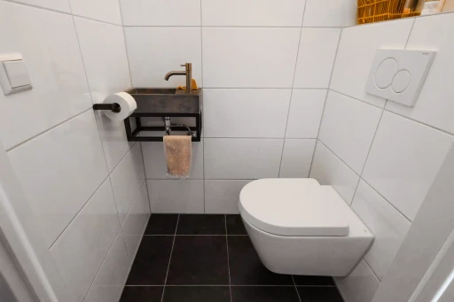 Het aparte toilet met een wandcloset, een kleine fontein en witte wandtegels.