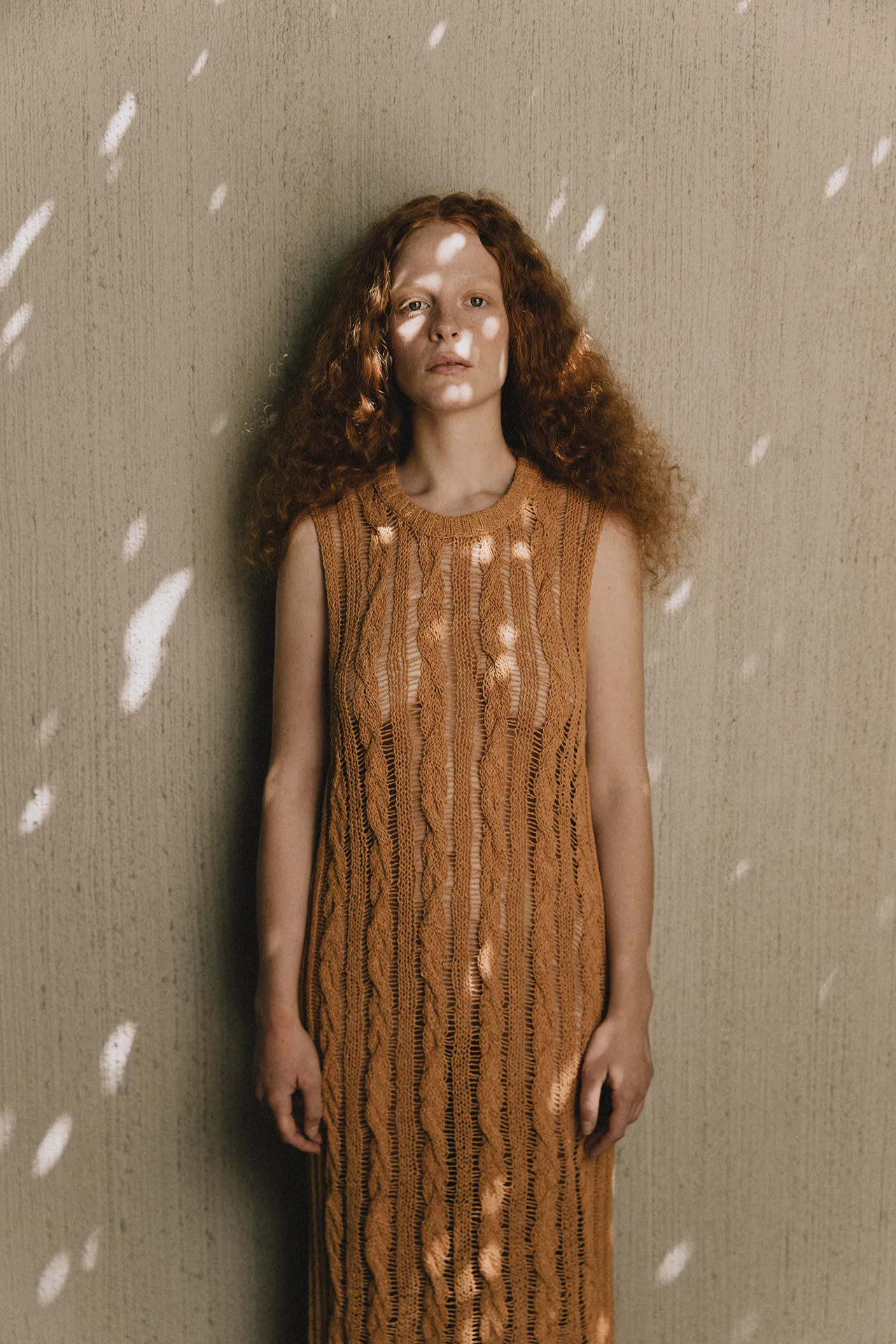 Full-length view of Annapurna SS26 collection golden-brown sleeveless maxi dress with vertical cable knitting and sheer open-stitch textures.