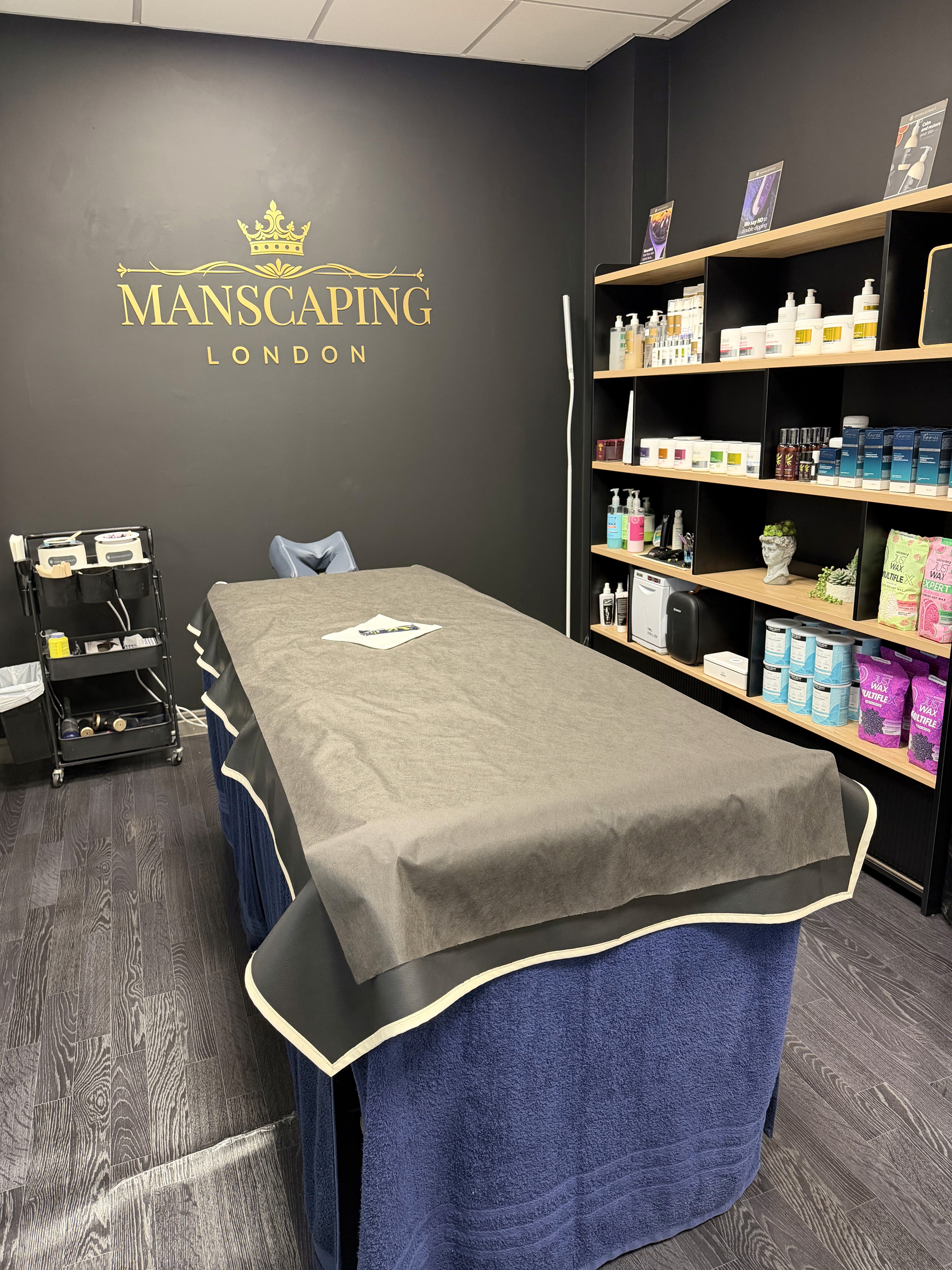 Treatments space in the Manscaping salon, featuring long table in the middle, long shelf with products on the right, waxing station on the left and the manscaping logo on the wall