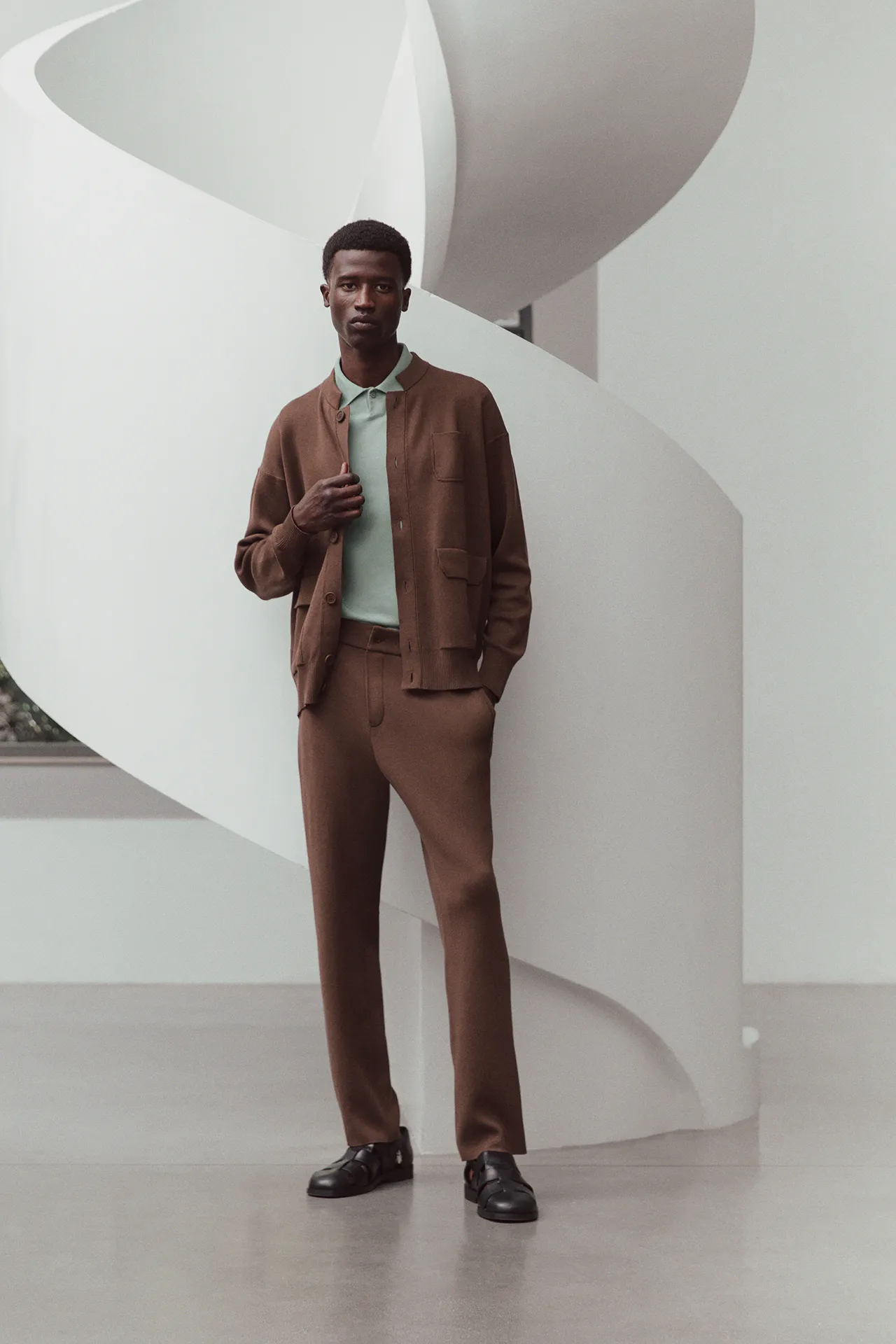 Full-length view of Aida Barni SS26 collection men's brown knit cardigan and trousers set, paired with a light green polo shirt.