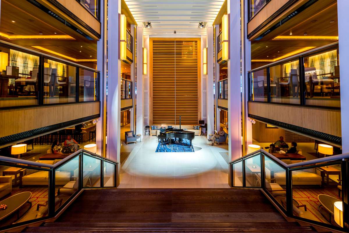 A modern hotel lobby with symmetrical seating areas, warm lighting, and a central lounge area featuring a blue rug.