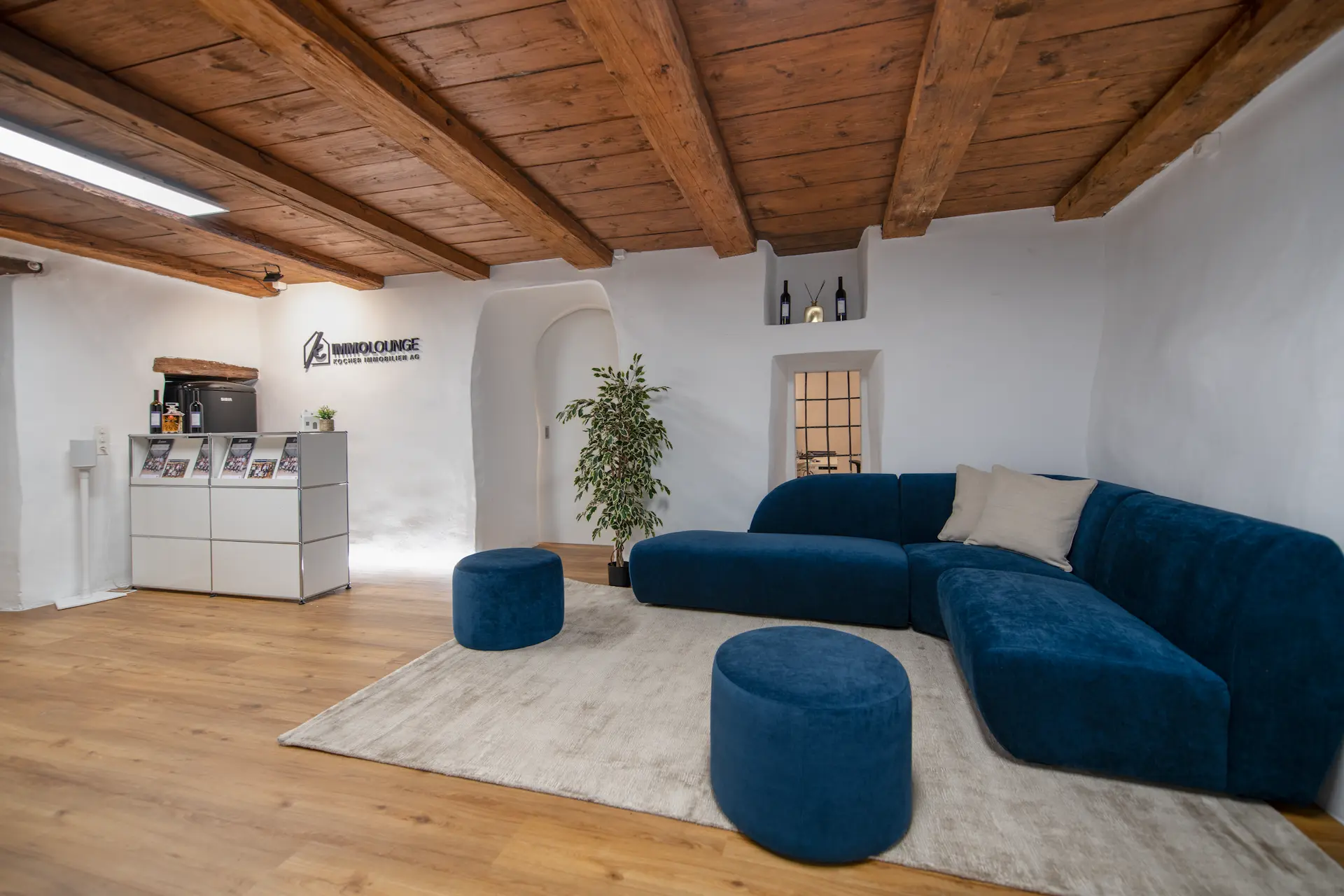 Moderne Immolounge von Kocher Immobilien mit blauem Sofa und Holzdecke