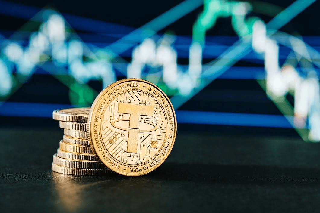 Goldene Tether-Münzen vor einem unscharfen Marktchart als Sinnbild für die Rolle von USDT in Tethers Zahlungsambitionen.