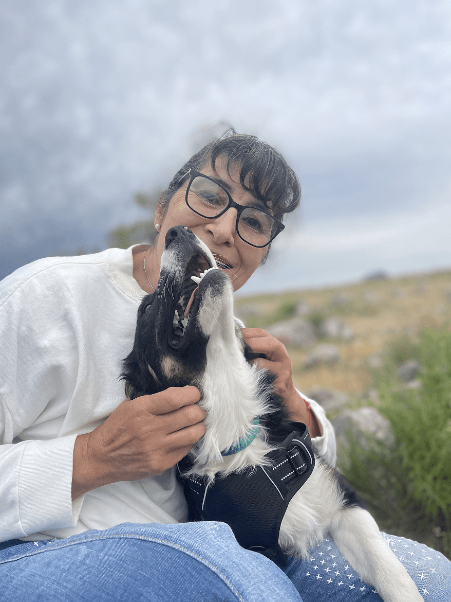 A person stands outdoors in a natural setting with lush green trees under a clear sky, wearing a dark sweatshirt, and looking into the distance.