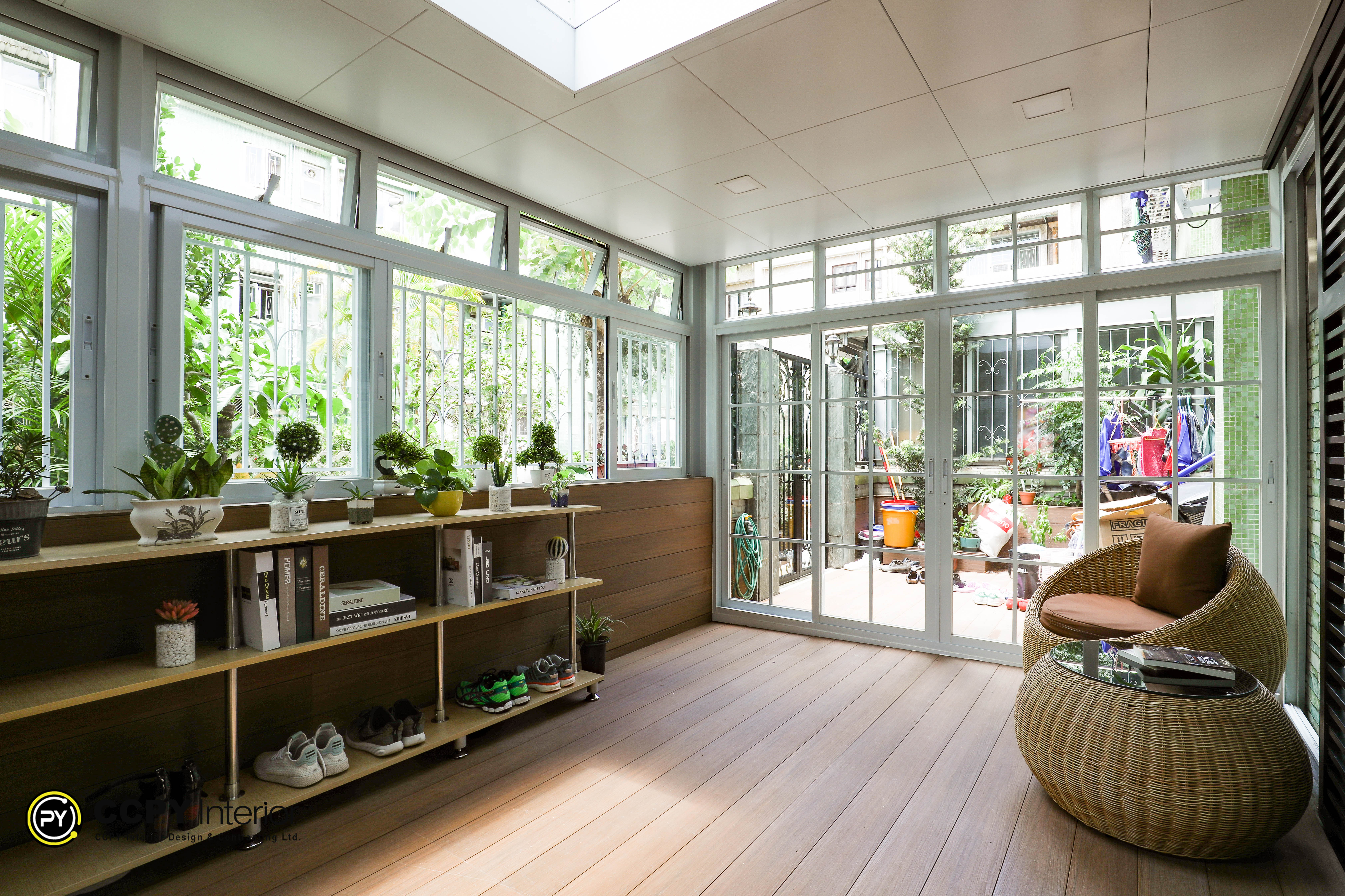 Sunroom lounge area with rattan wicker chairs, skylights, exposed industrial-style metal bookshelves, and light wood flooring in Kwan Lok Sun Chuen.