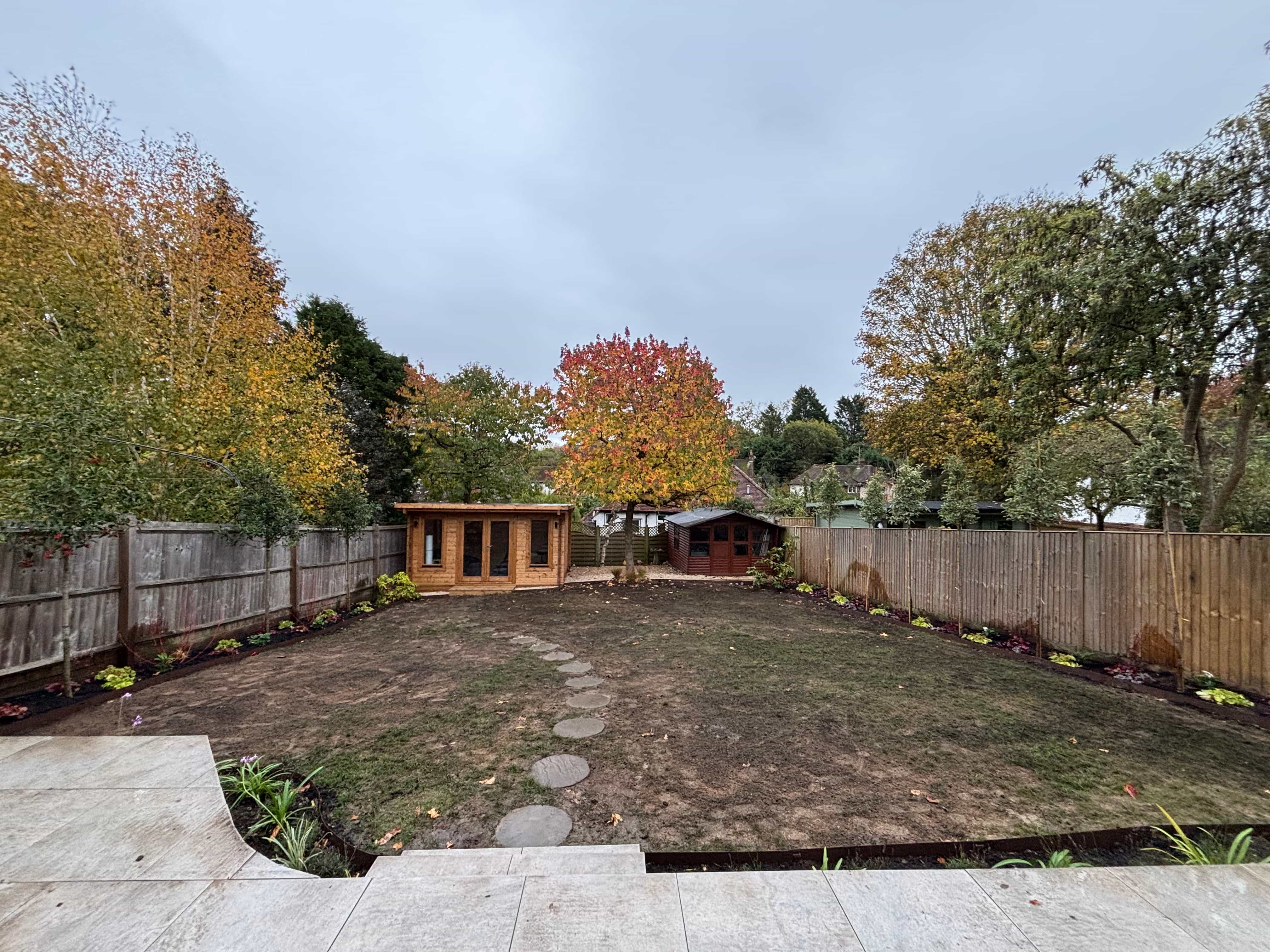 : Garden path through modern black wooden pergolas leading to a green shed.