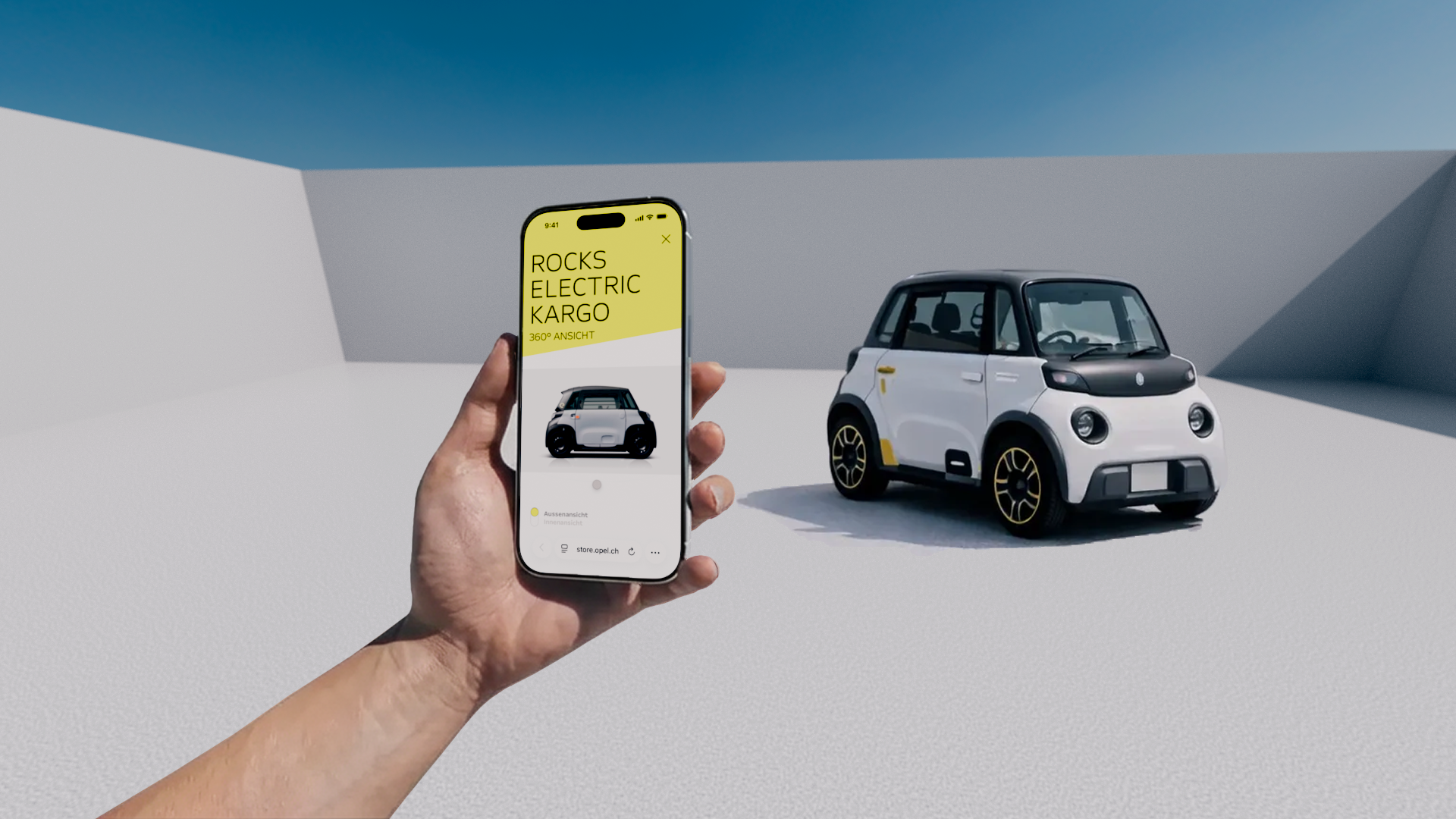 Eine Hand hält ein Smartphone, auf dem der Schweizer Online-Shop für den Opel Rocks Electric zu sehen ist. Dahinter steht das Auto. 