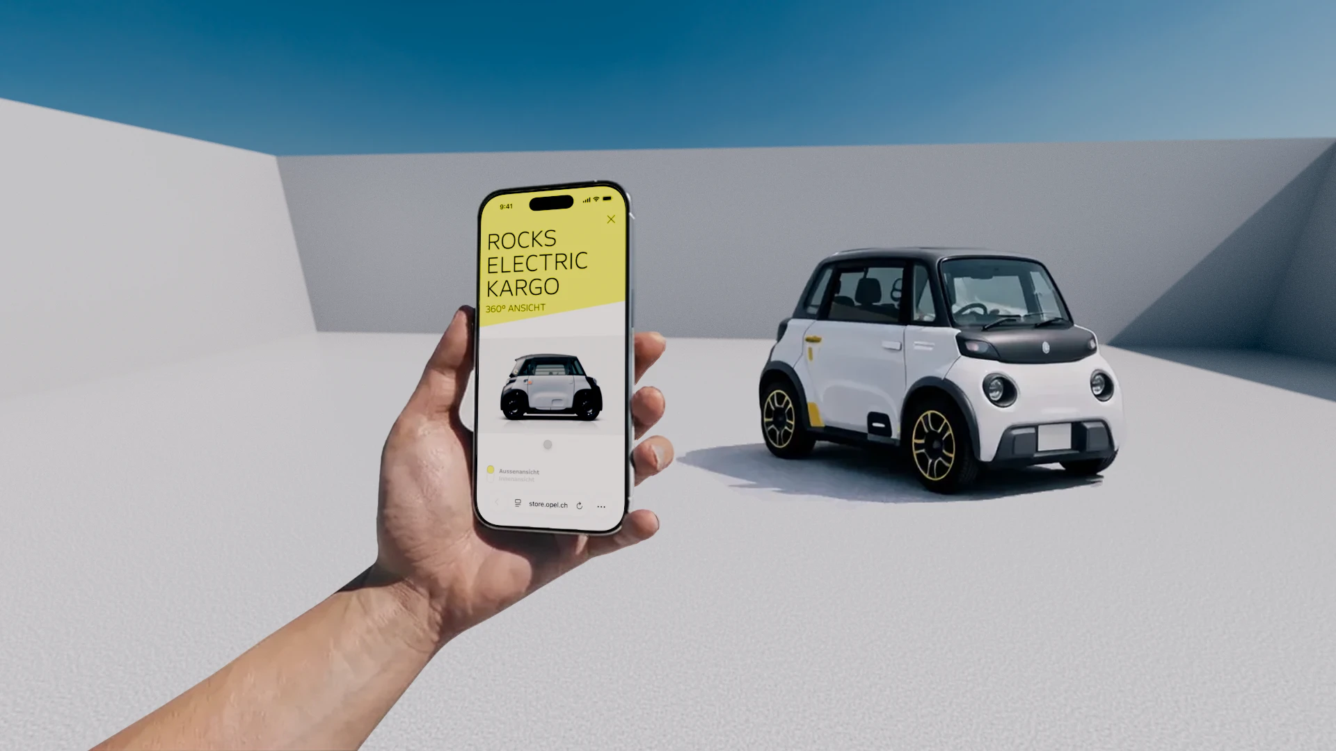 Eine Hand hält ein Smartphone, auf dem der Schweizer Online-Shop für den Opel Rocks Electric zu sehen ist. Dahinter steht das Auto. 
