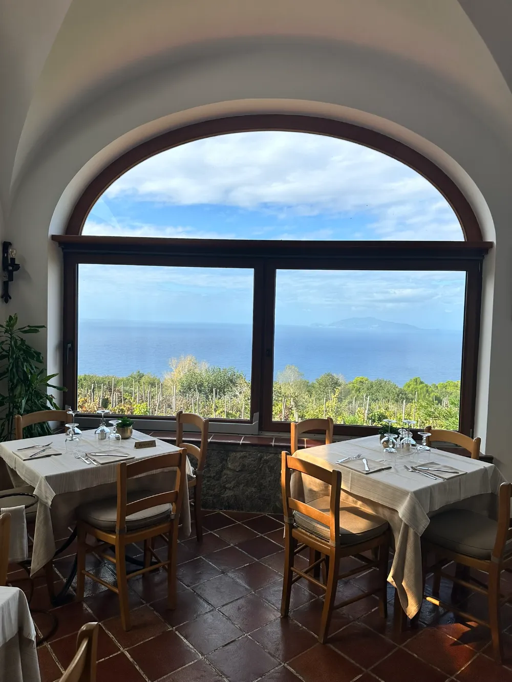 A restaurant dining room on Capri with a large arched window looking out over the sea.