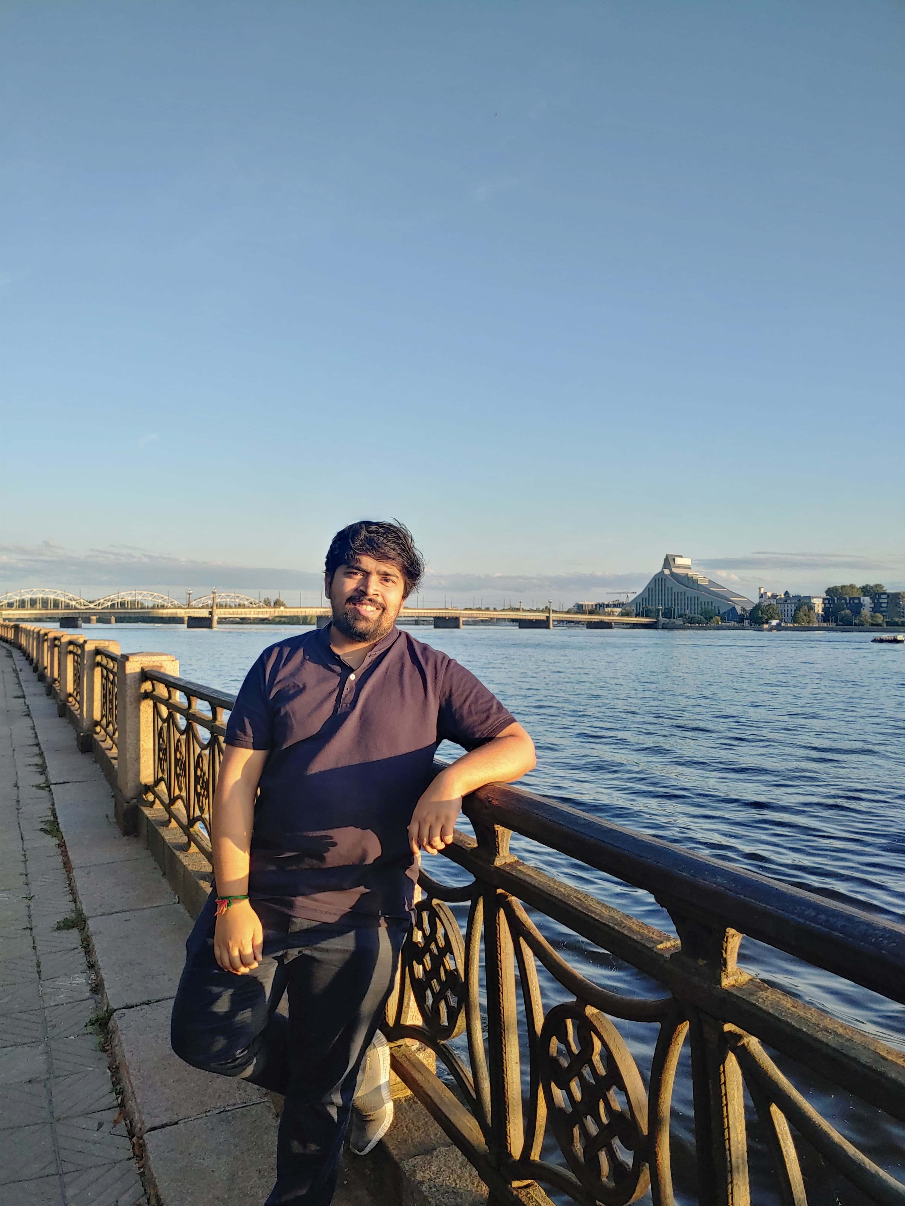 Picture of myself standing by a river leaning on a rail, smiling at the camera