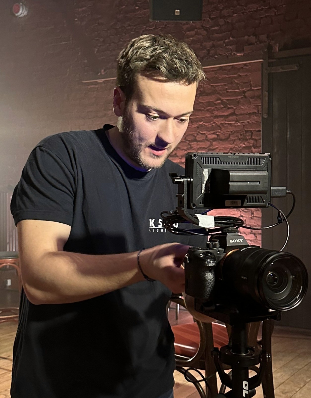 A woman with short curly hair wearing a black t-shirt looks into the camera.