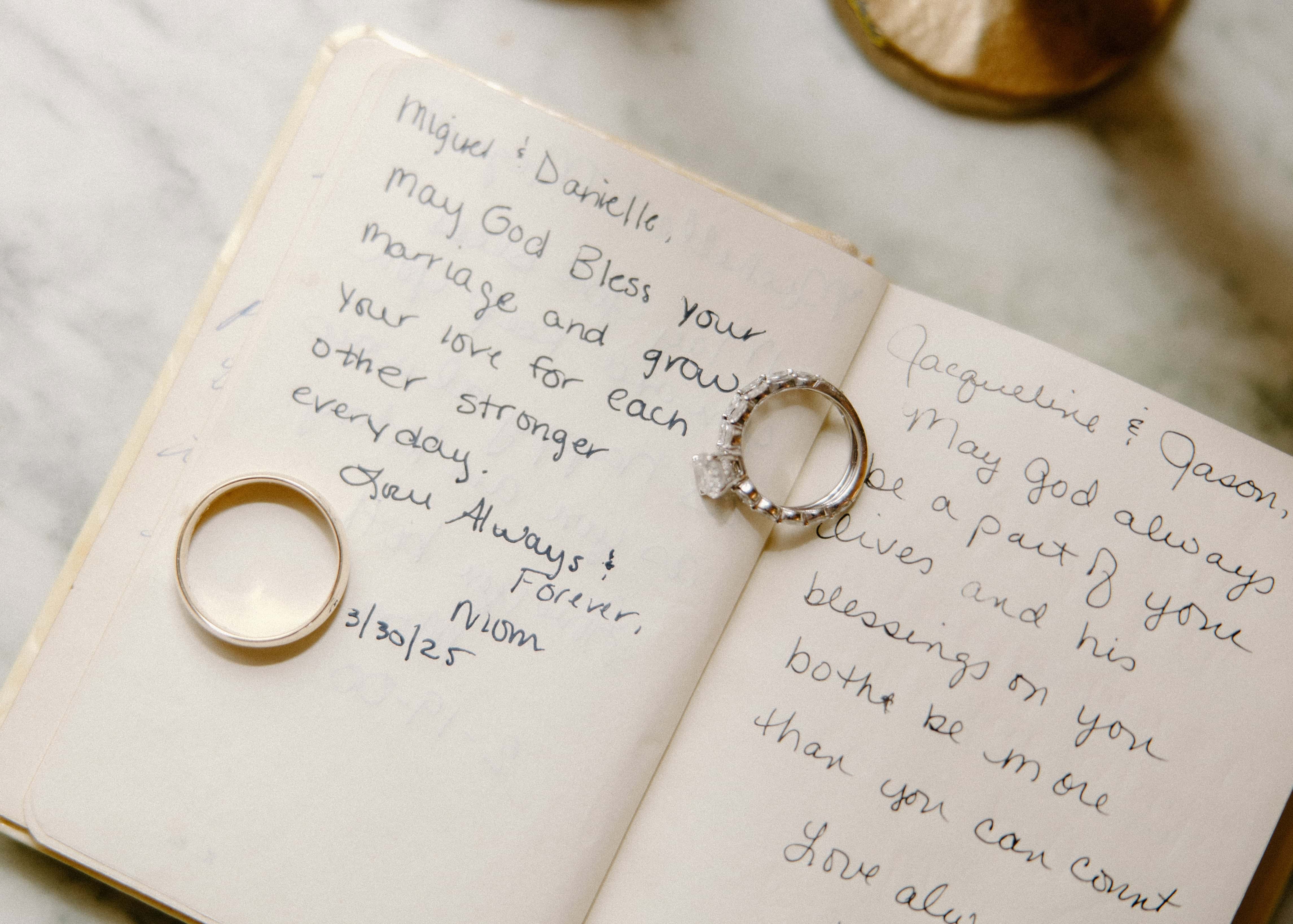 A close-up shot of a pair of wedding rings resting on an open book with handwritten text.