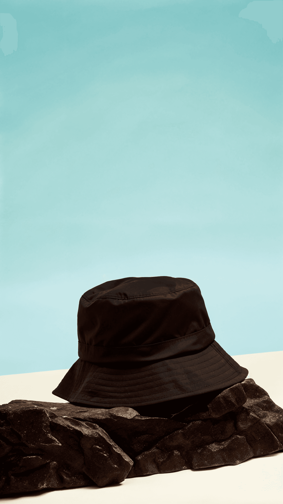 A black bucket hat resting on a rock, set against a soft blue background.