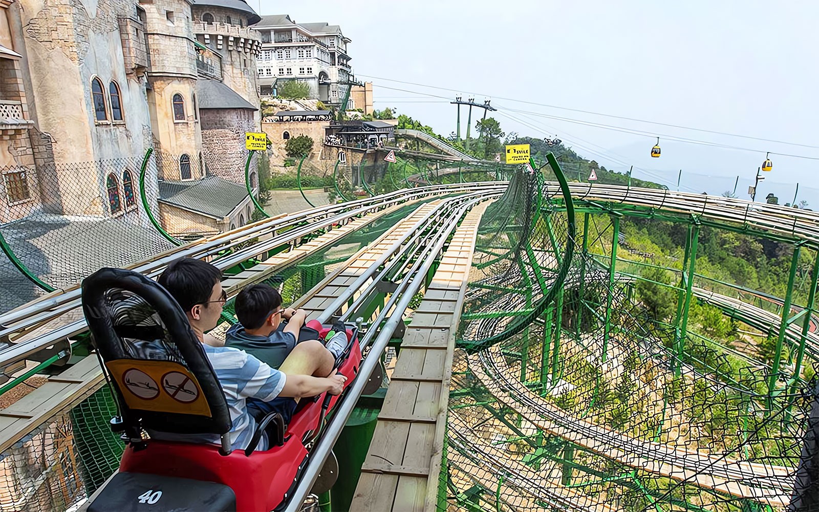 Father and child on Alpine Coaster at Ba Na Hills, Vietnam, with scenic view.
