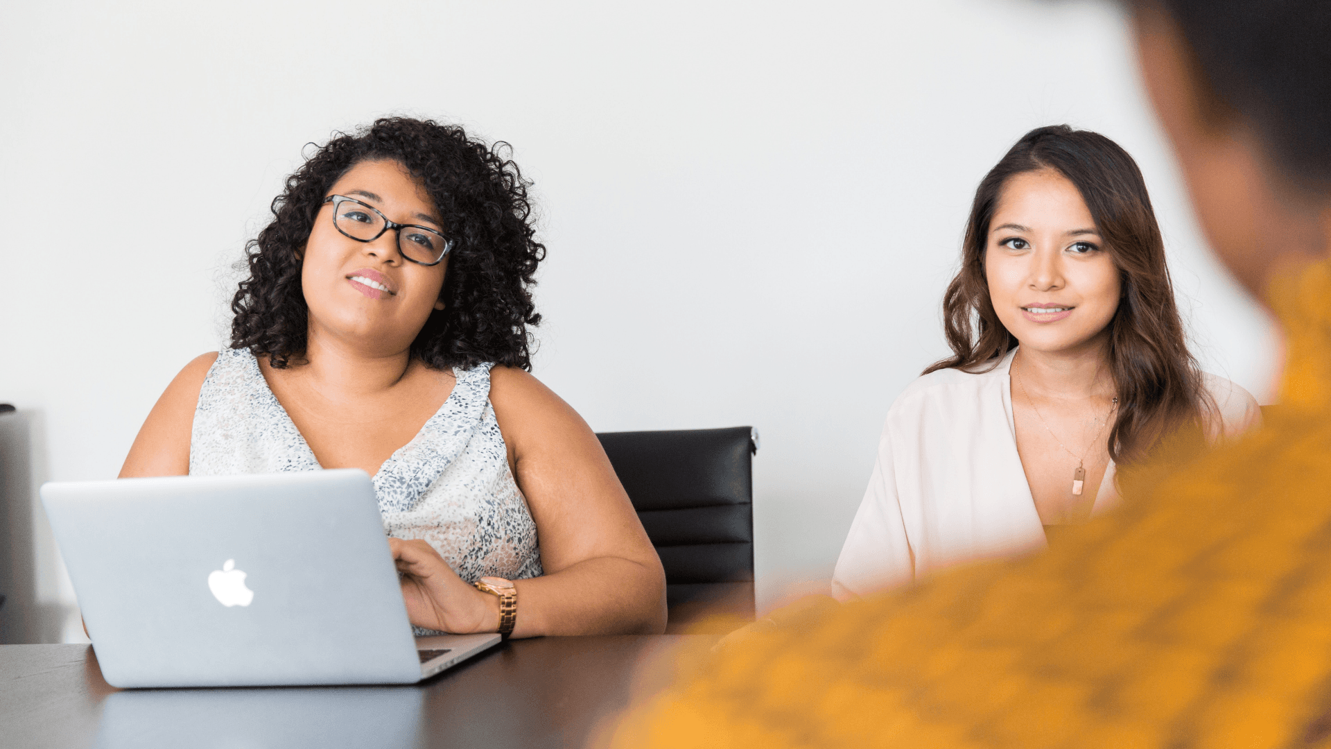 Two women sit facing a third person in a business meeting