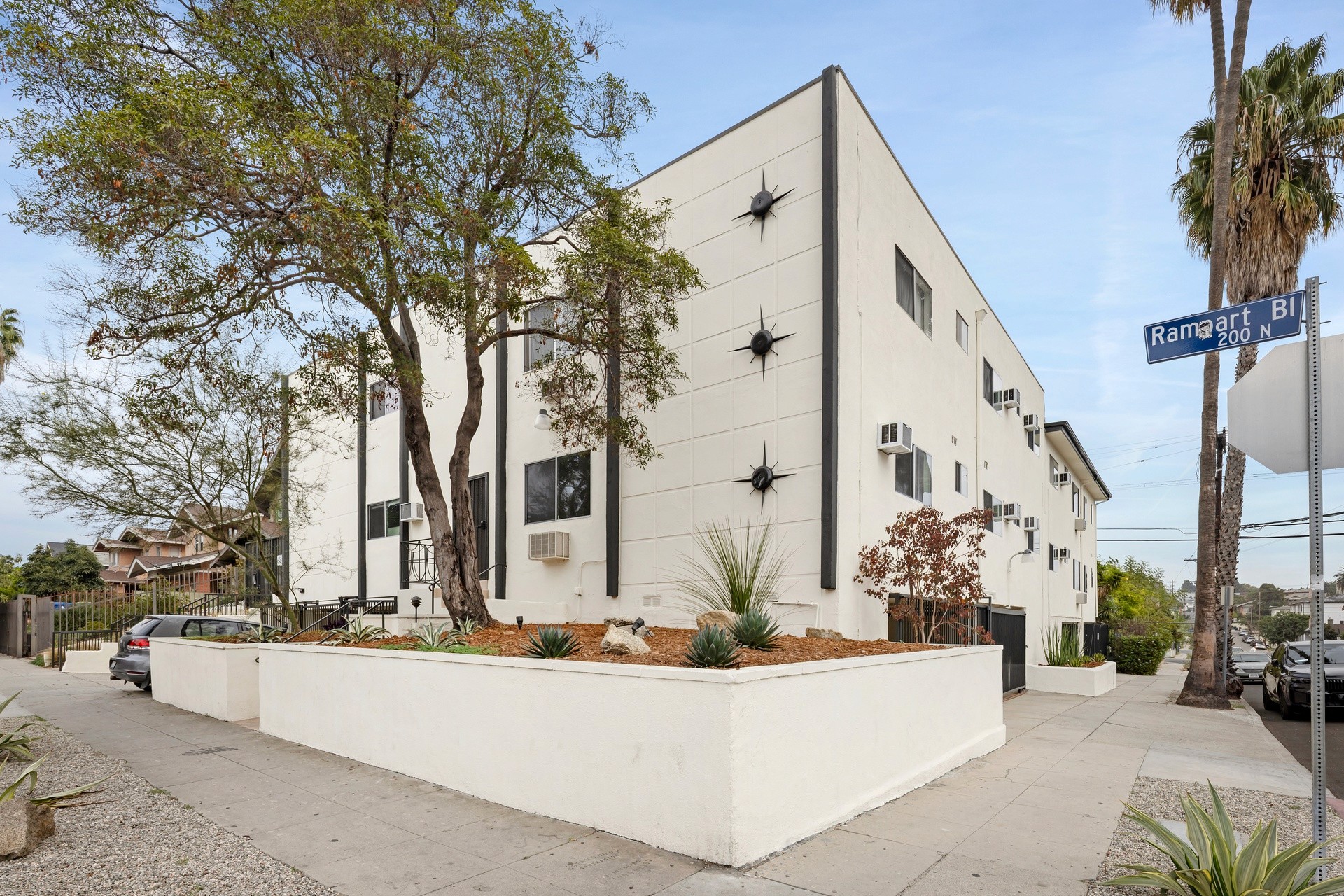 200 N Rampart exterior corner view with modern white facade, raised planters and mature trees.