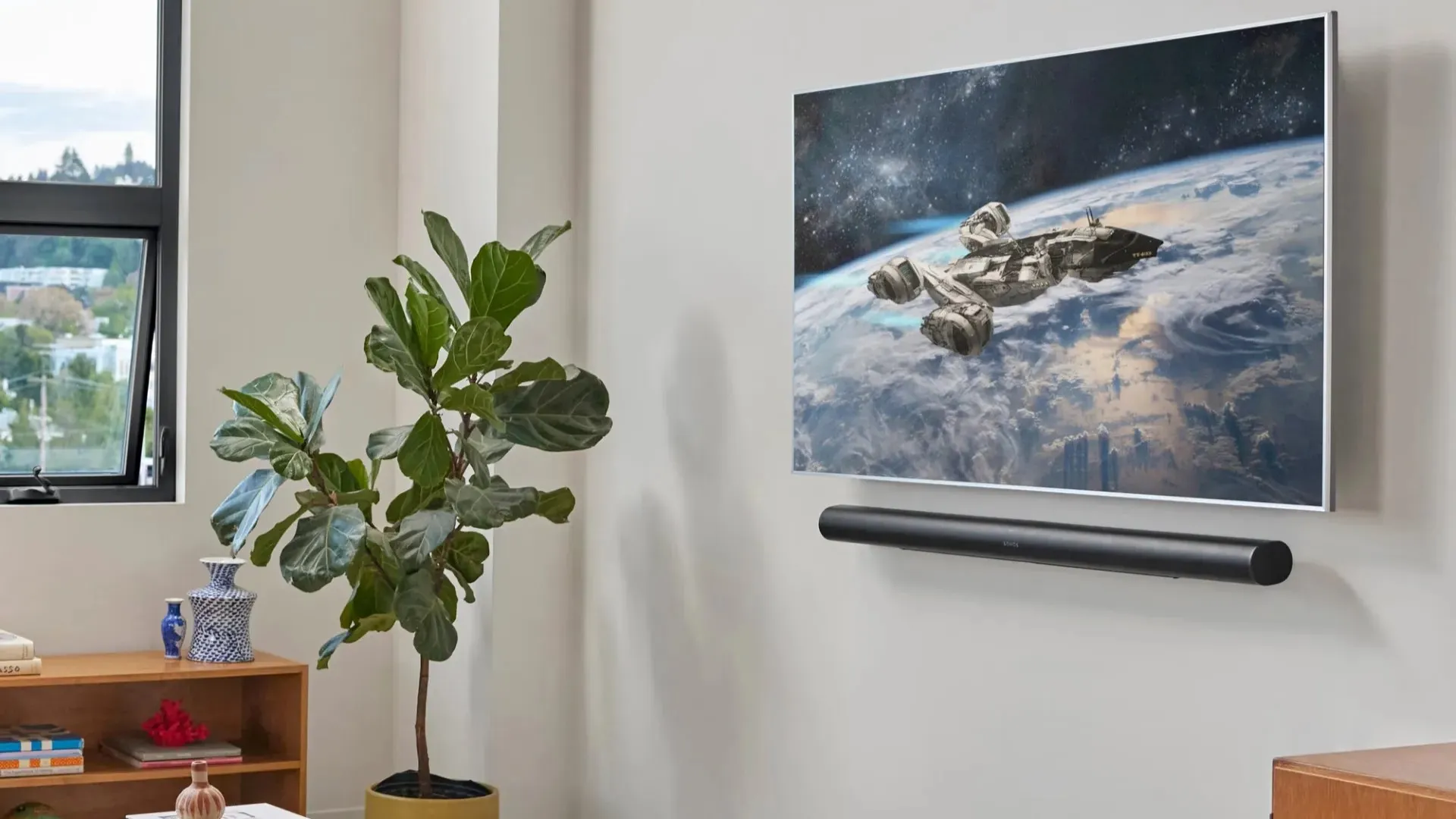 A sleek, modern living room features a wall-mounted flat-screen TV displaying a vibrant image of a spaceship above Earth, complemented by a stylish soundbar beneath and a lush green potted plant beside a wooden shelf with decorative items.
