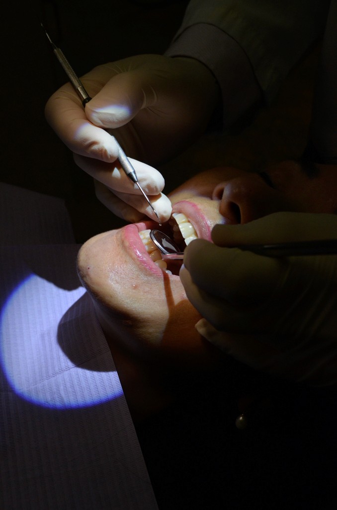 A dental professional performing a preventive care procedure on a patient's teeth, illuminated by a bright light.