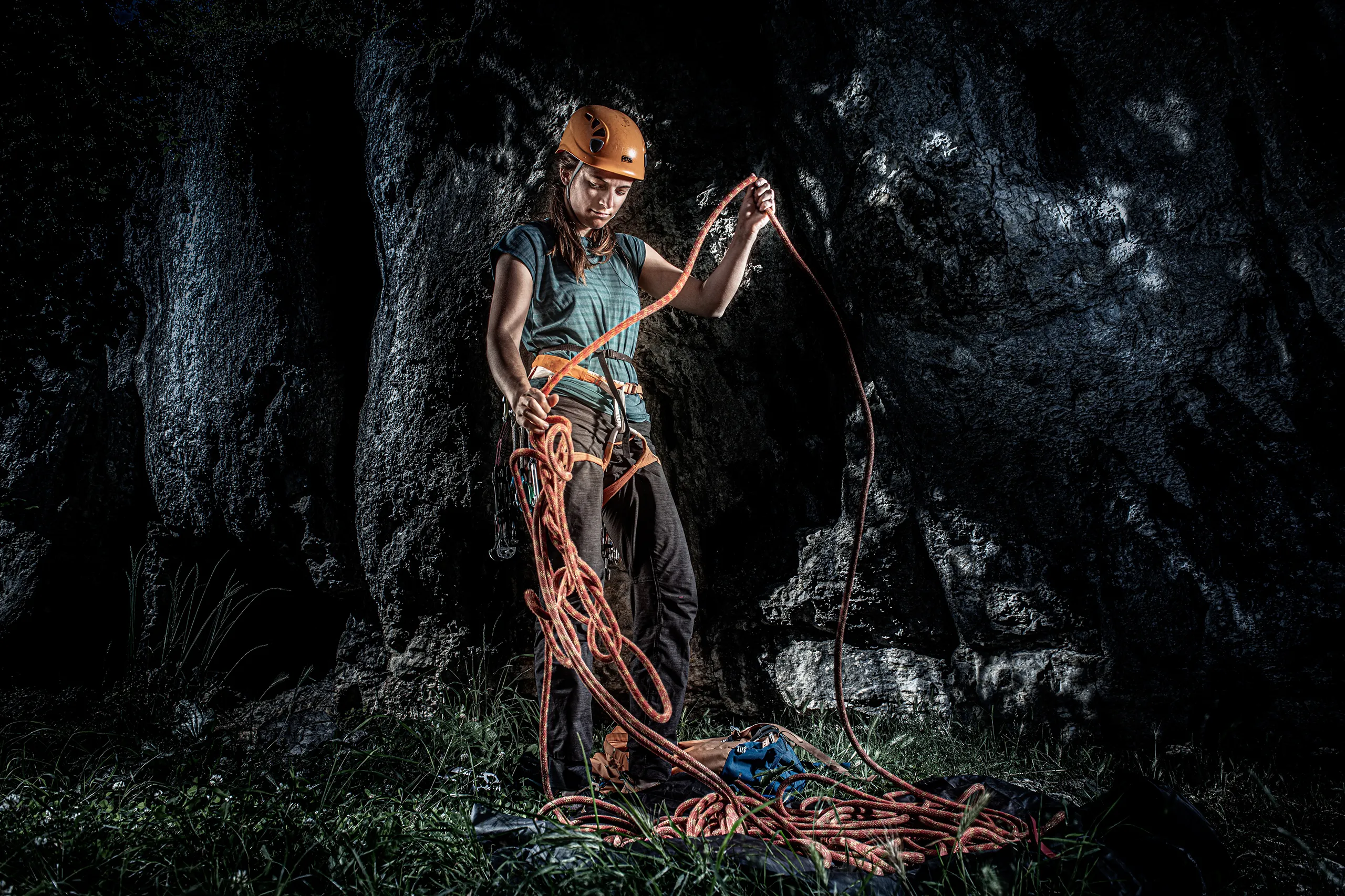 A cinematic portrait of a female climber in a helmet holding climbing ropes against a dark rock face.