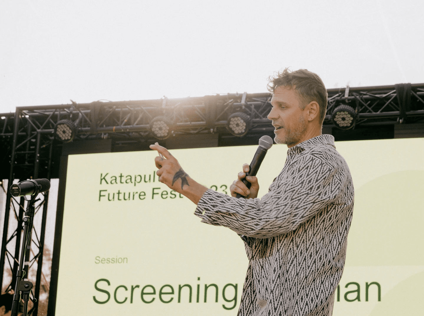 Festival speaker on stage standing in front of a backdrop design featuring the logo design made for the event, with bright colours and big typography.