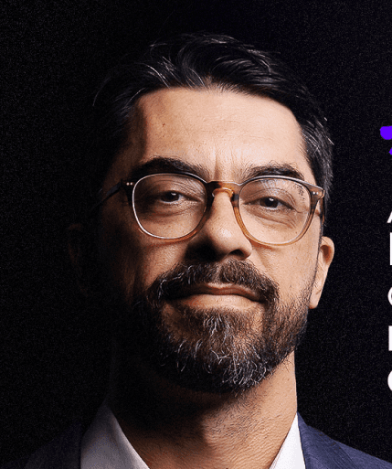 Close-up portrait of a freckled woman with soft pink hair and star earring, natural light, white tank top.