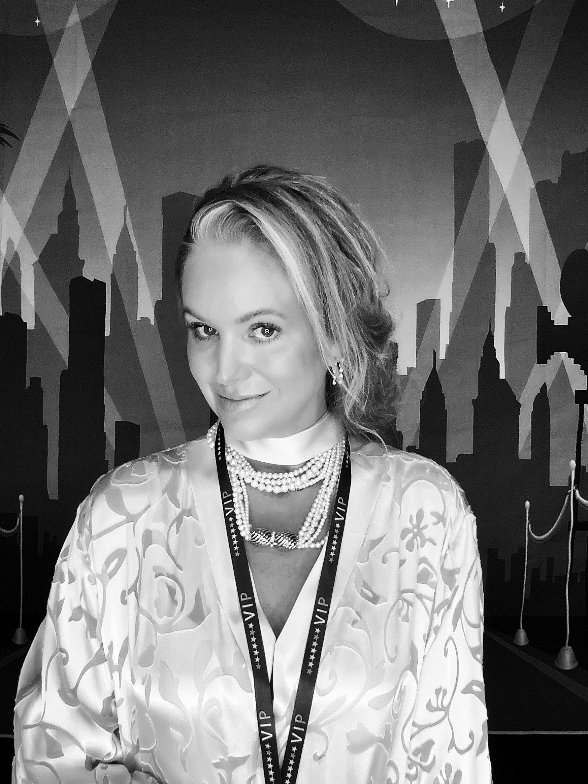 A woman wearing a patterned satin robe and a VIP lanyard stands confidently against a backdrop of a stylized city skyline with dramatic lighting effects.