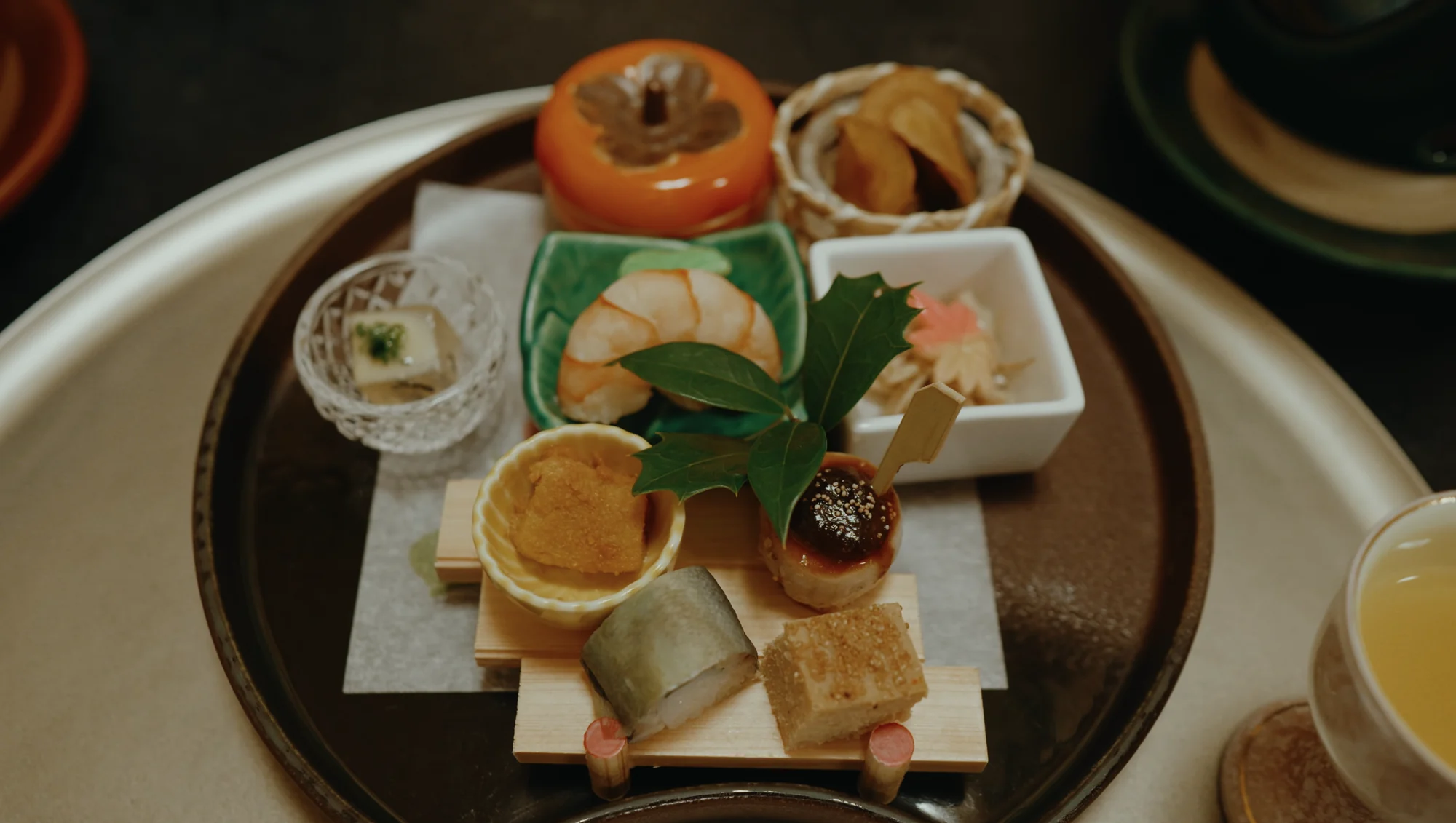 A lacquer tray of kaiseki dishes including a persimmon-shell vessel and grilled items