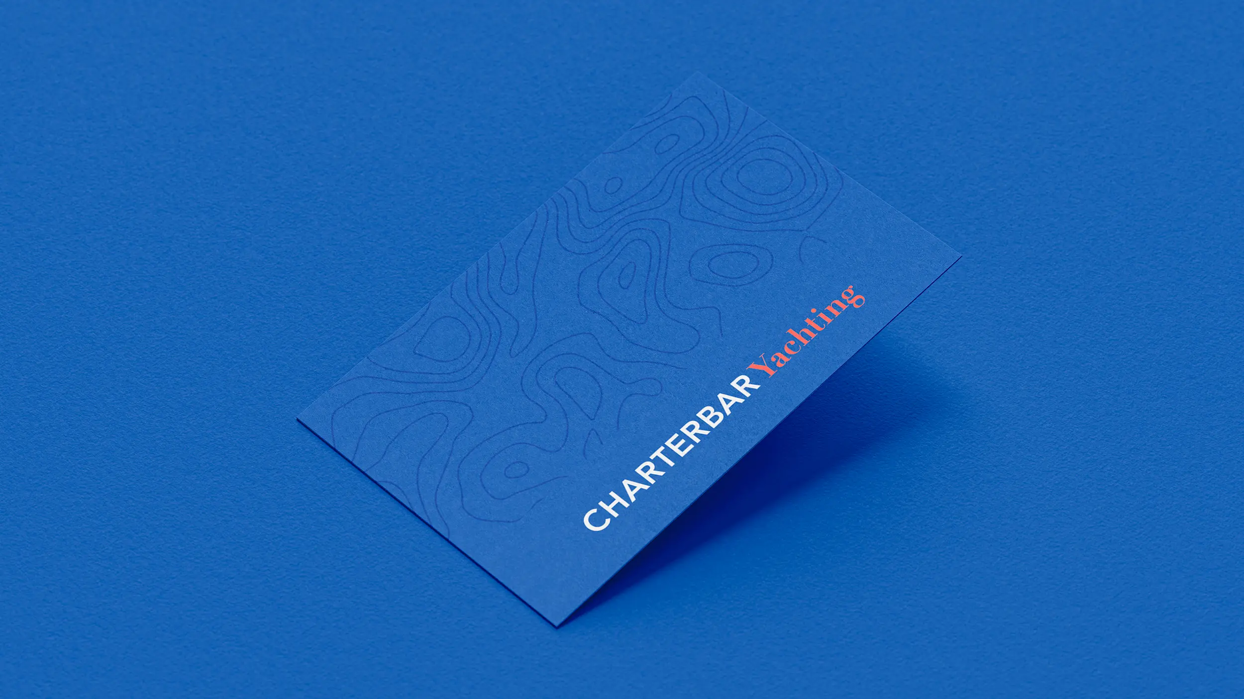 Blaue Visitenkarte mit Topografielinien und Schriftzug „CHARTERBAR Yachting“ in Weiß und Orange.