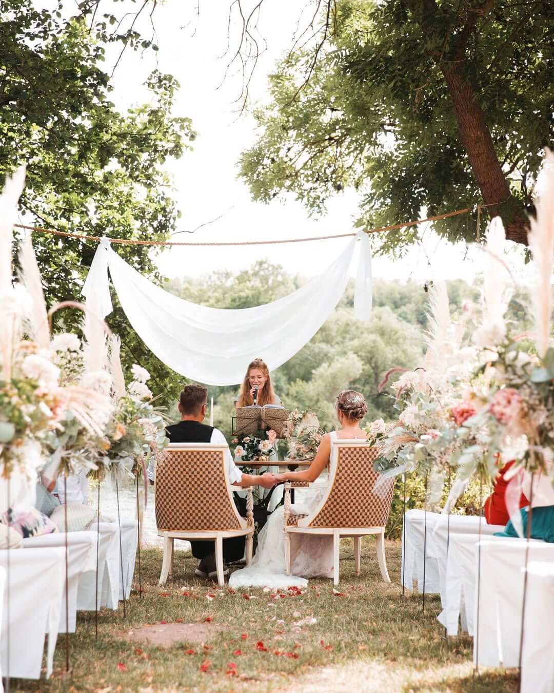 Brautpaar bei Zeremonie im Freien, mit Blumenarrangements und Rednerpult. Hochzeitsfeier im Garten.