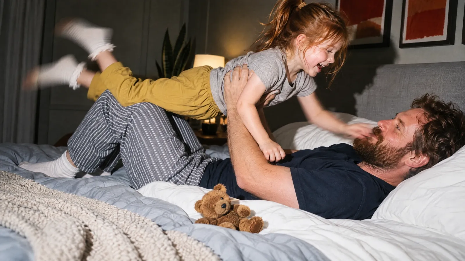 A dad lifting his laughing daughter above him on the bed